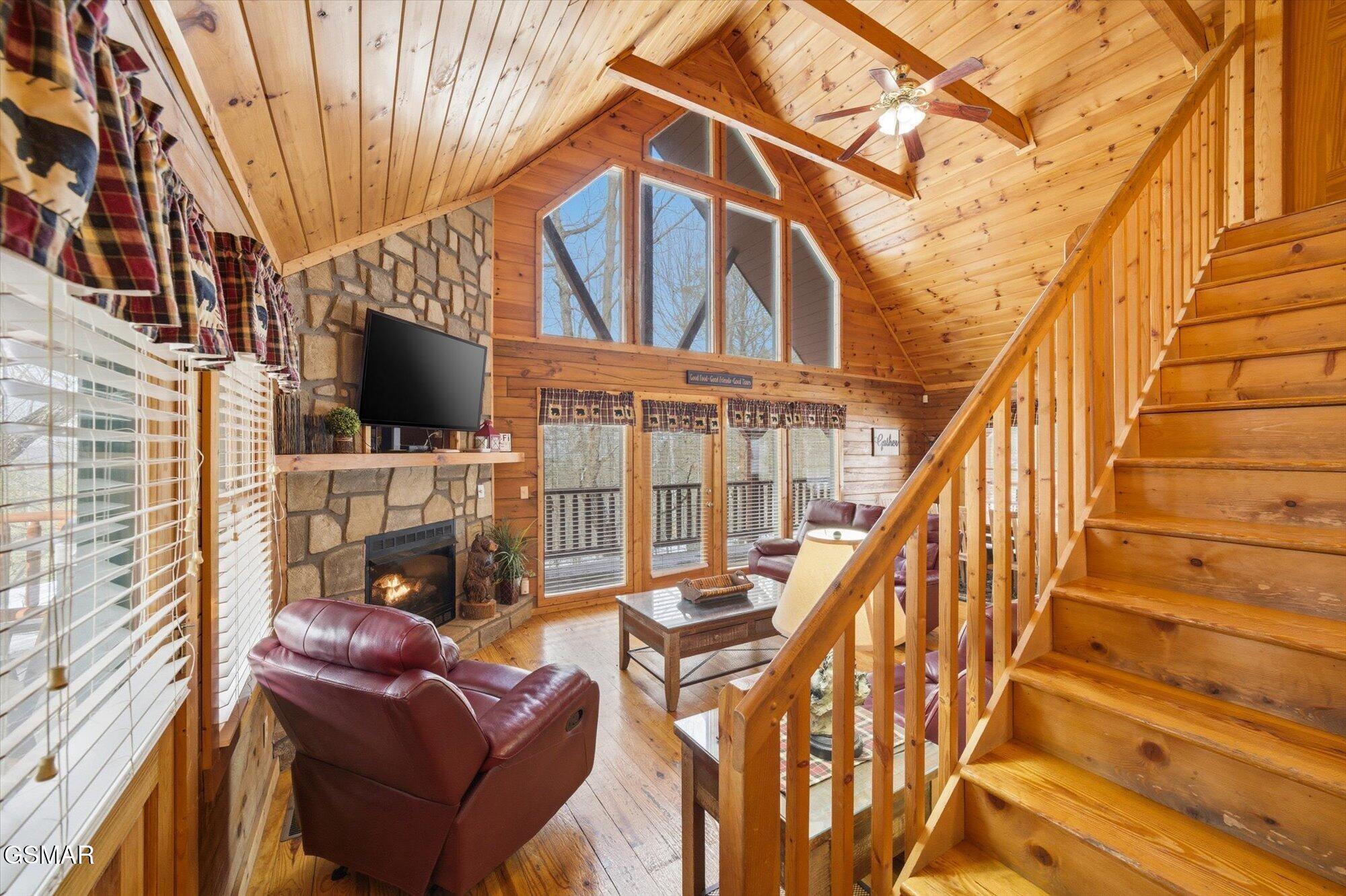 Cabin living room with vaulted wood ceiling, stone fireplace, leather seating, and staircase.