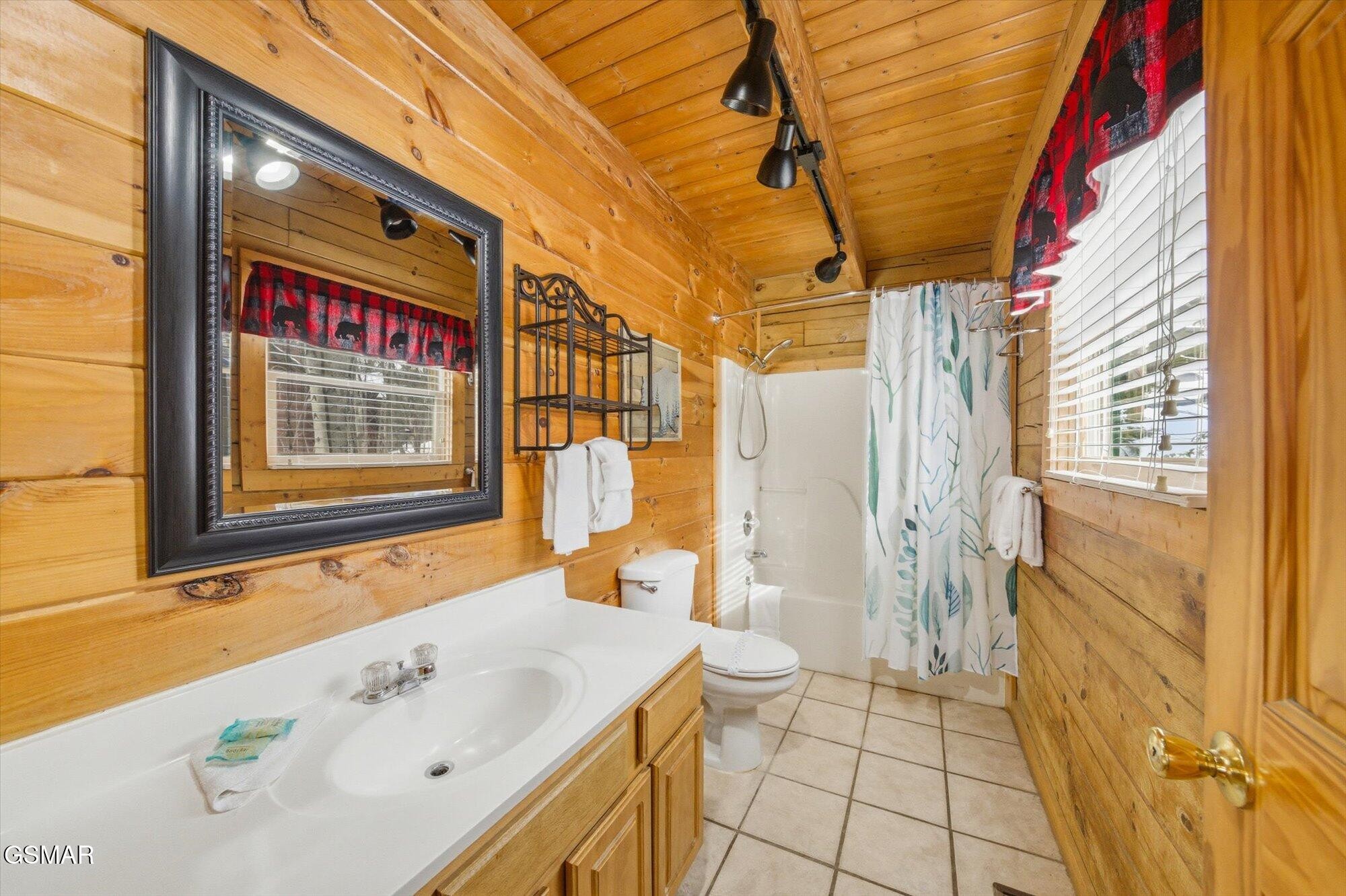 Cabin bathroom with wood walls, a wood vanity, and a tub-shower with patterned curtain.