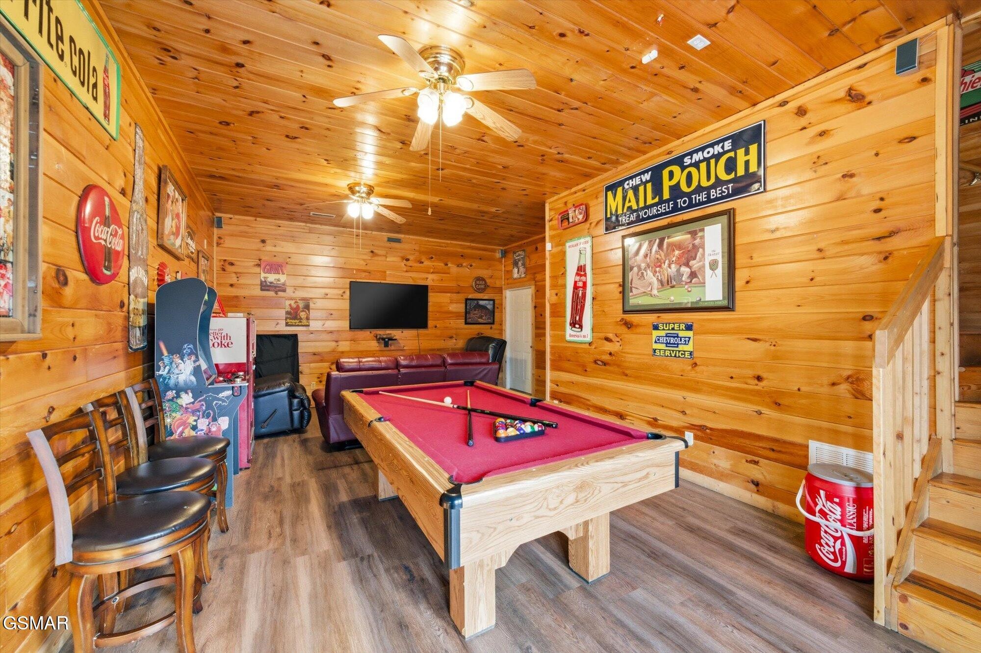 Wood-paneled game room with a red-felt pool table, arcade machine, and vintage advertising signs.