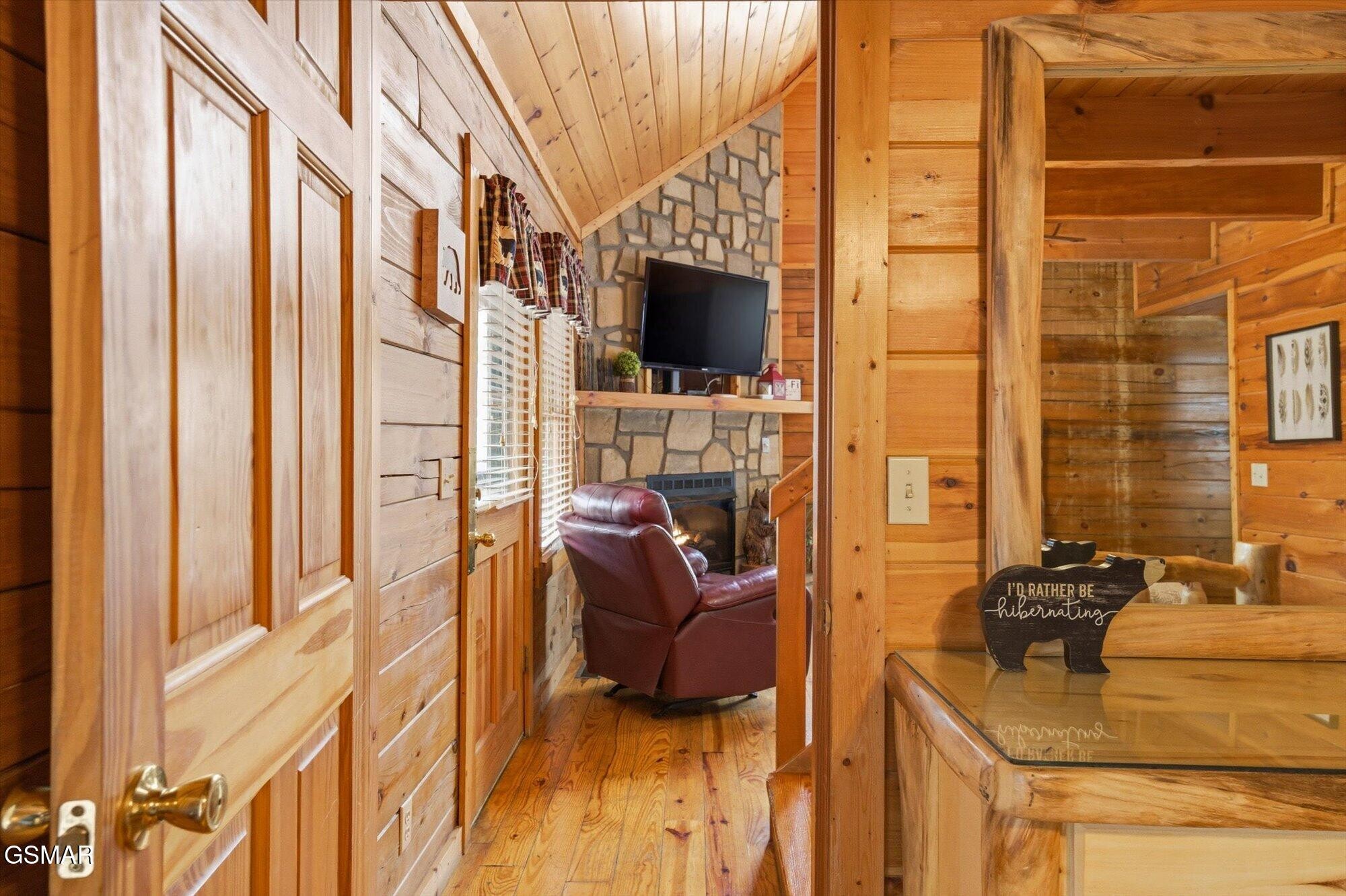 Cabin living room with a stone fireplace, vaulted wood ceiling, and leather recliner.