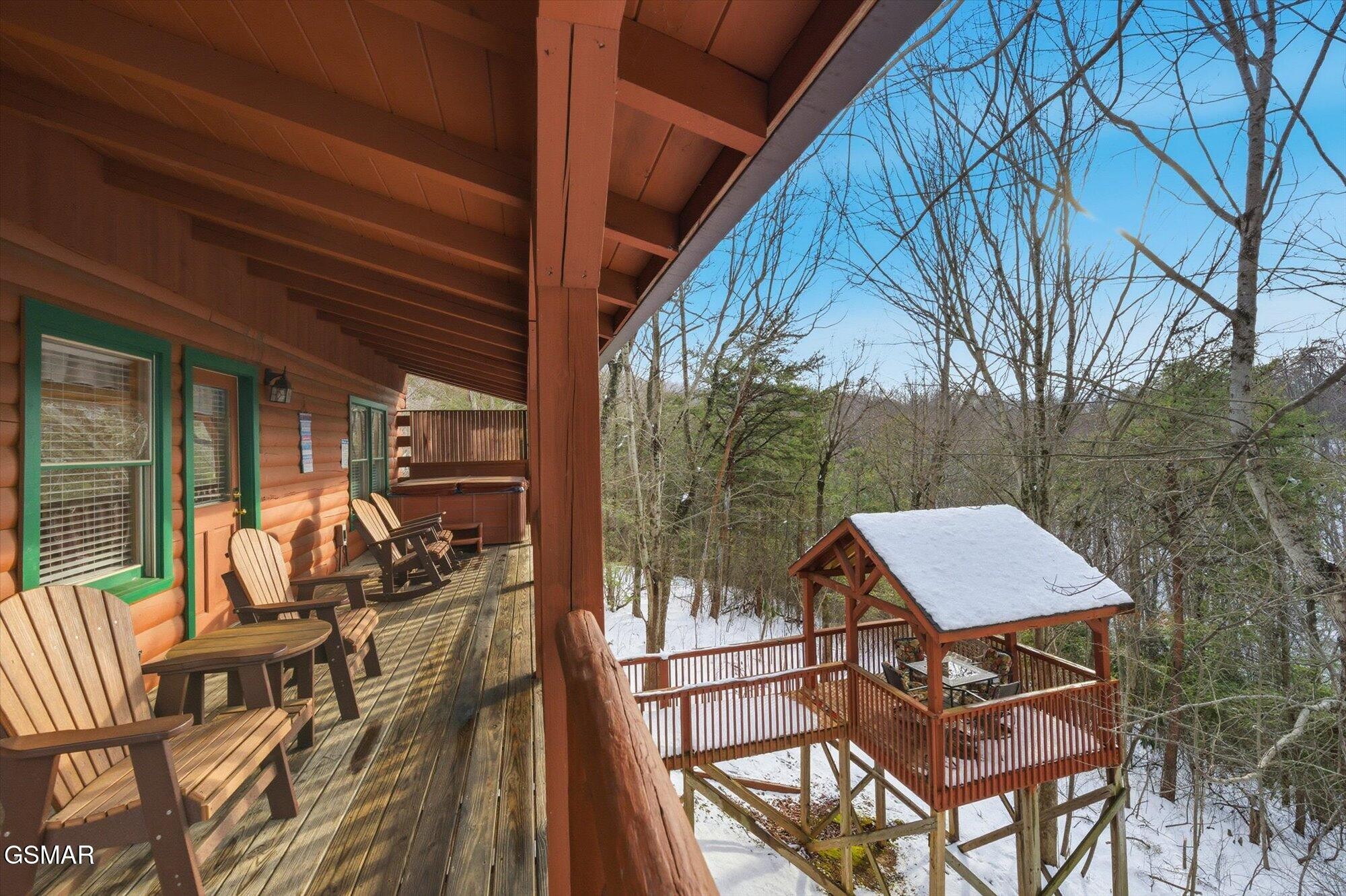 Cabin deck with Adirondack chairs overlooking a snowy wooded lot and raised gazebo.