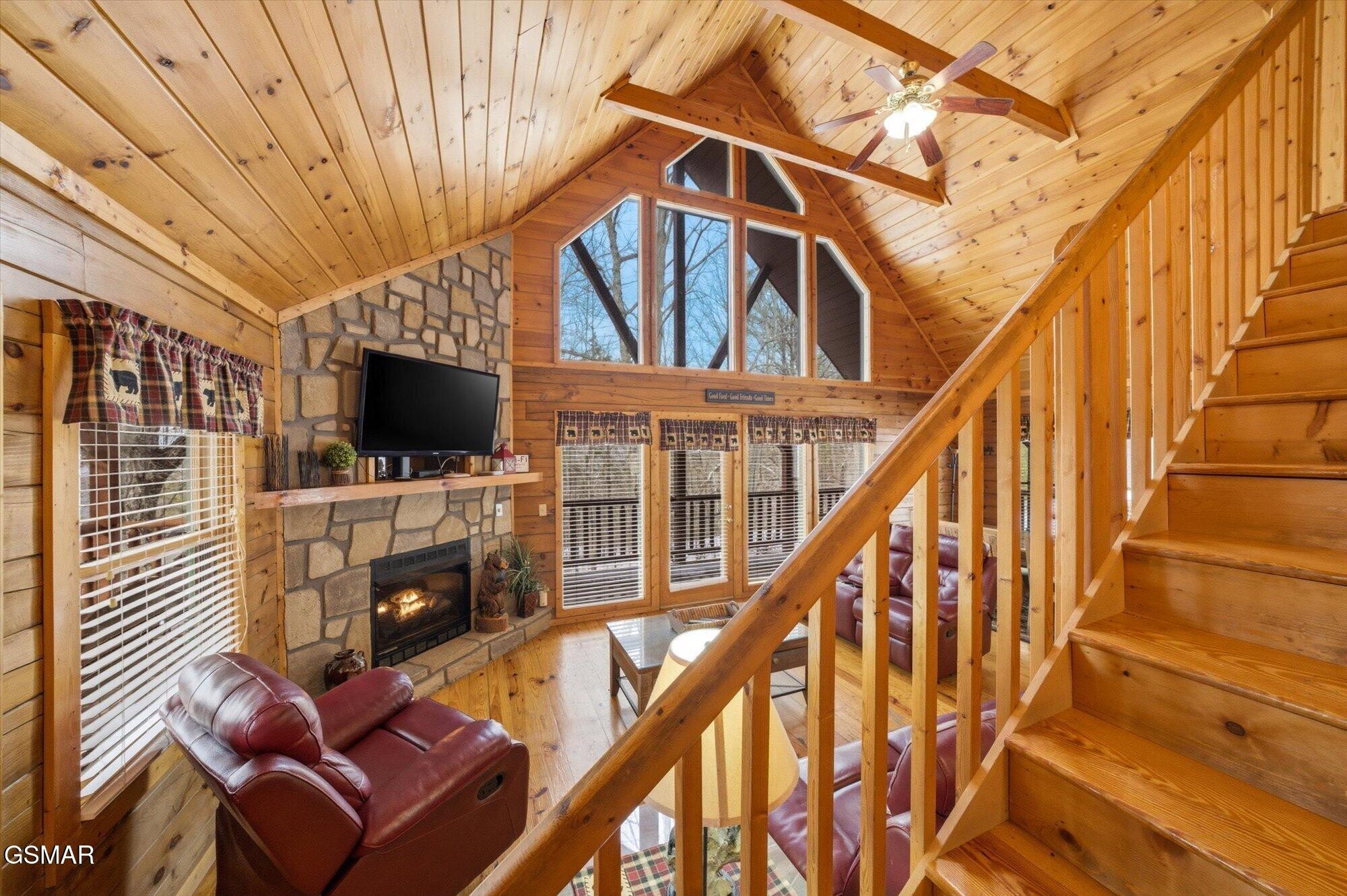 Cabin living room with a stone fireplace, vaulted wood ceiling, leather seating, and staircase to the loft.