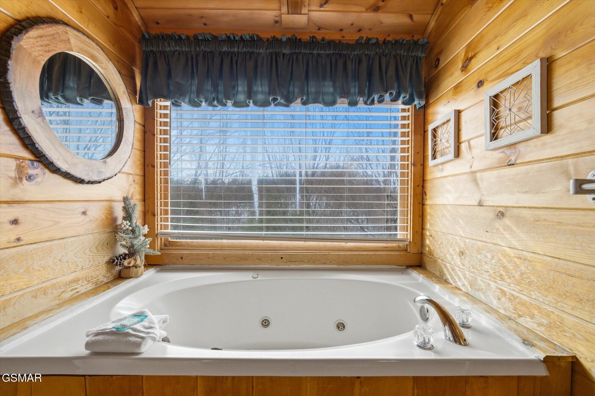 Jetted bathtub in a wood-paneled bathroom, with a wide window and rustic decor.