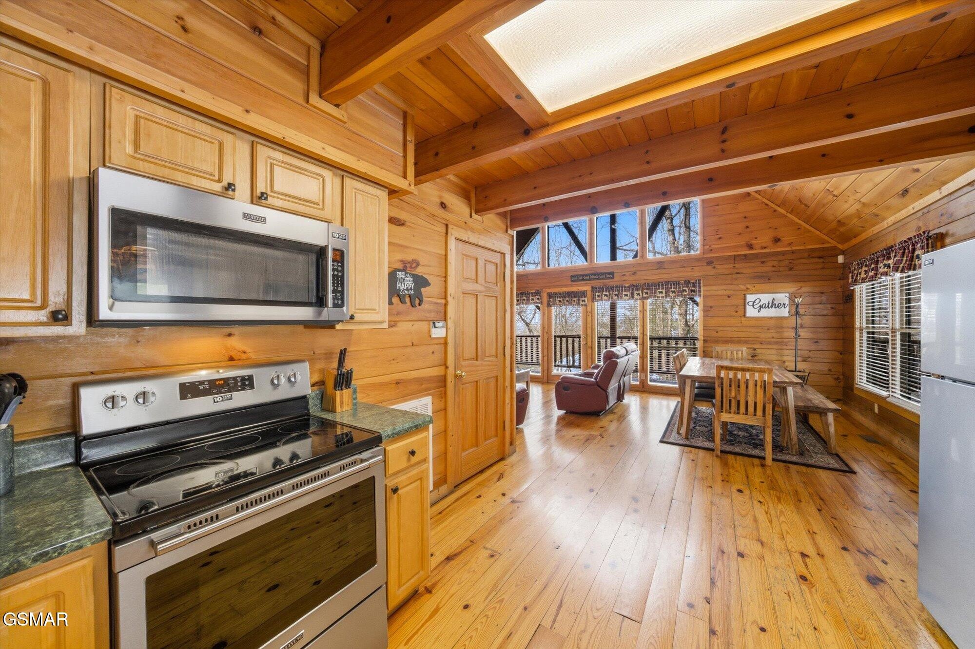 Cabin kitchen and dining area with knotty pine finishes, vaulted ceiling, and stainless steel appliances.