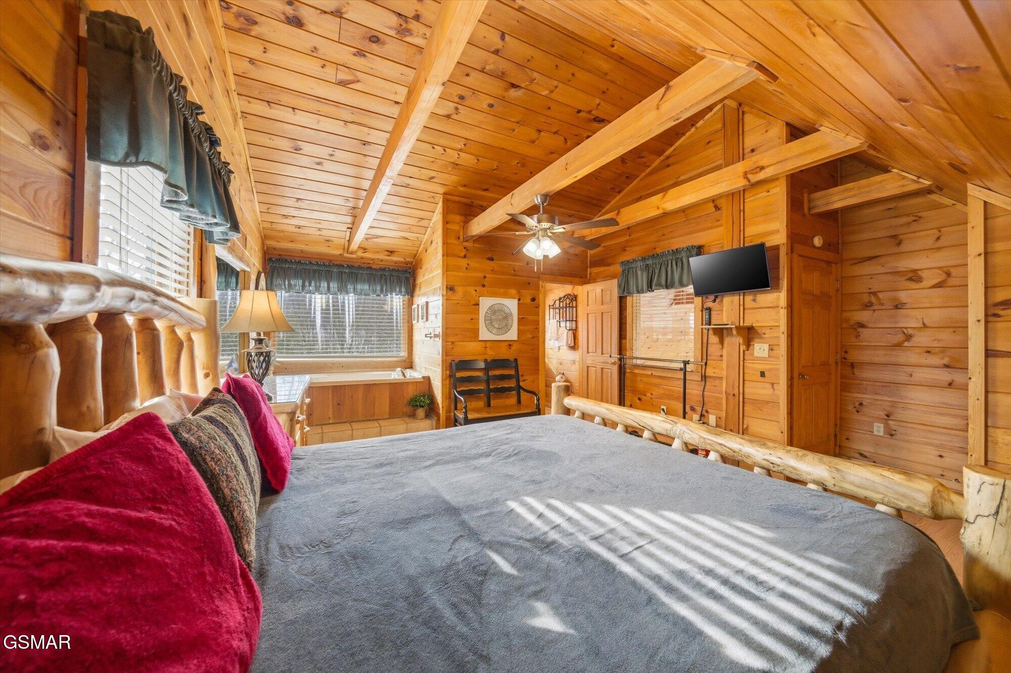 Log cabin bedroom with exposed timber beams, a large bed, and sunlight through window blinds.