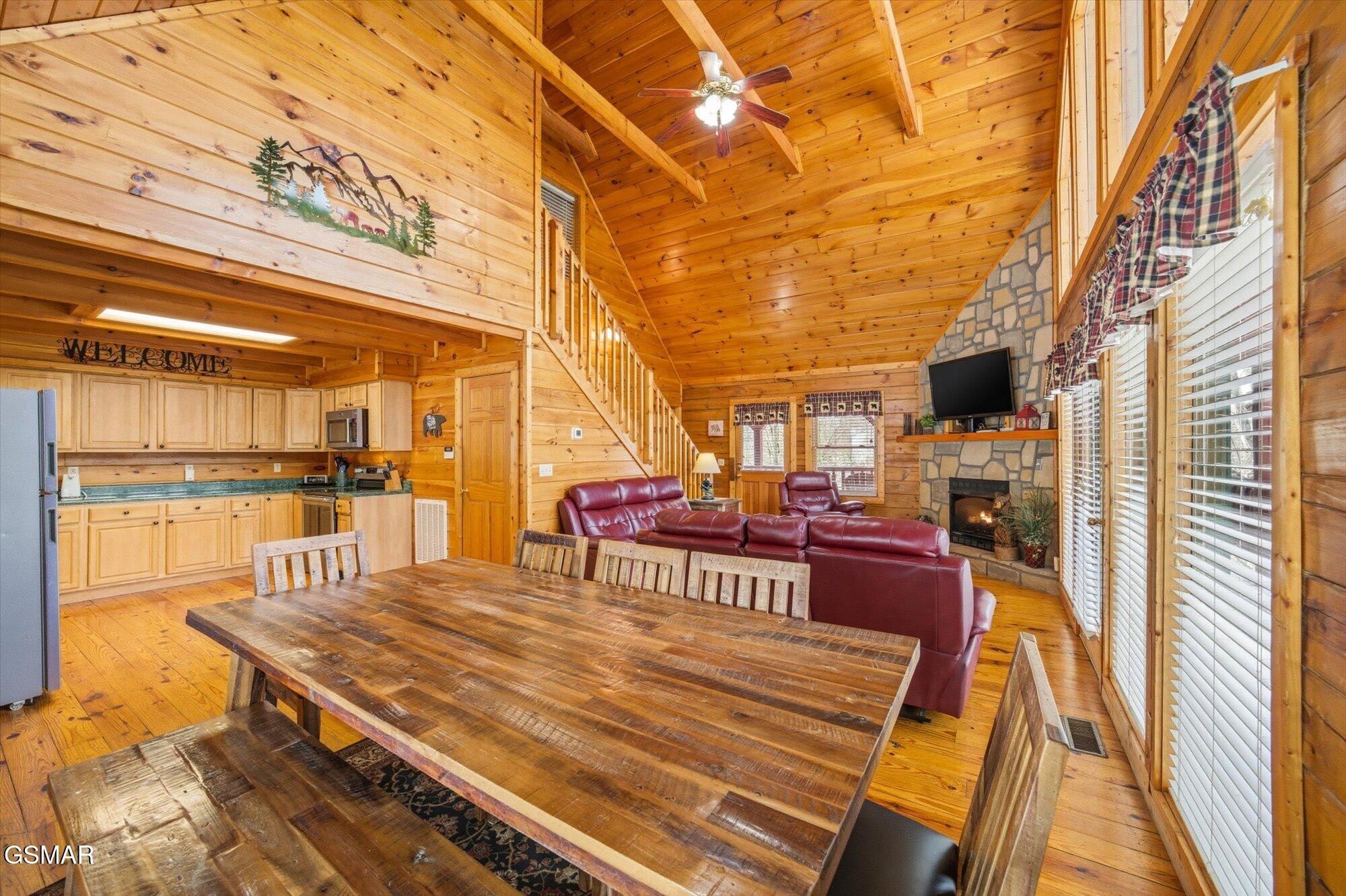 Open-plan cabin dining and living area with vaulted wood ceilings, red leather seating, and a stone fireplace.
