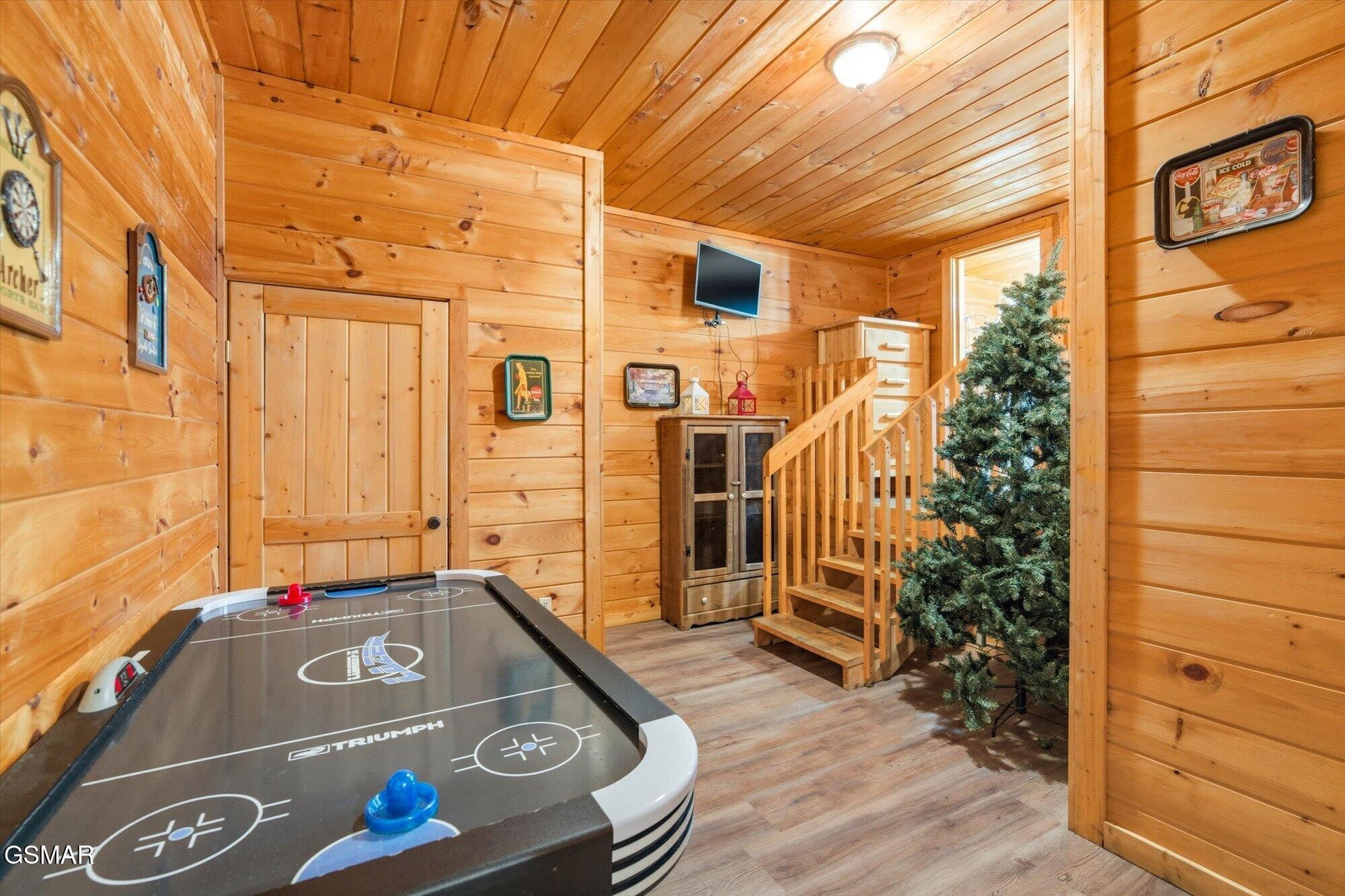 Wood-paneled game room with an air hockey table, staircase, beverage refrigerator, and artificial Christmas tree.