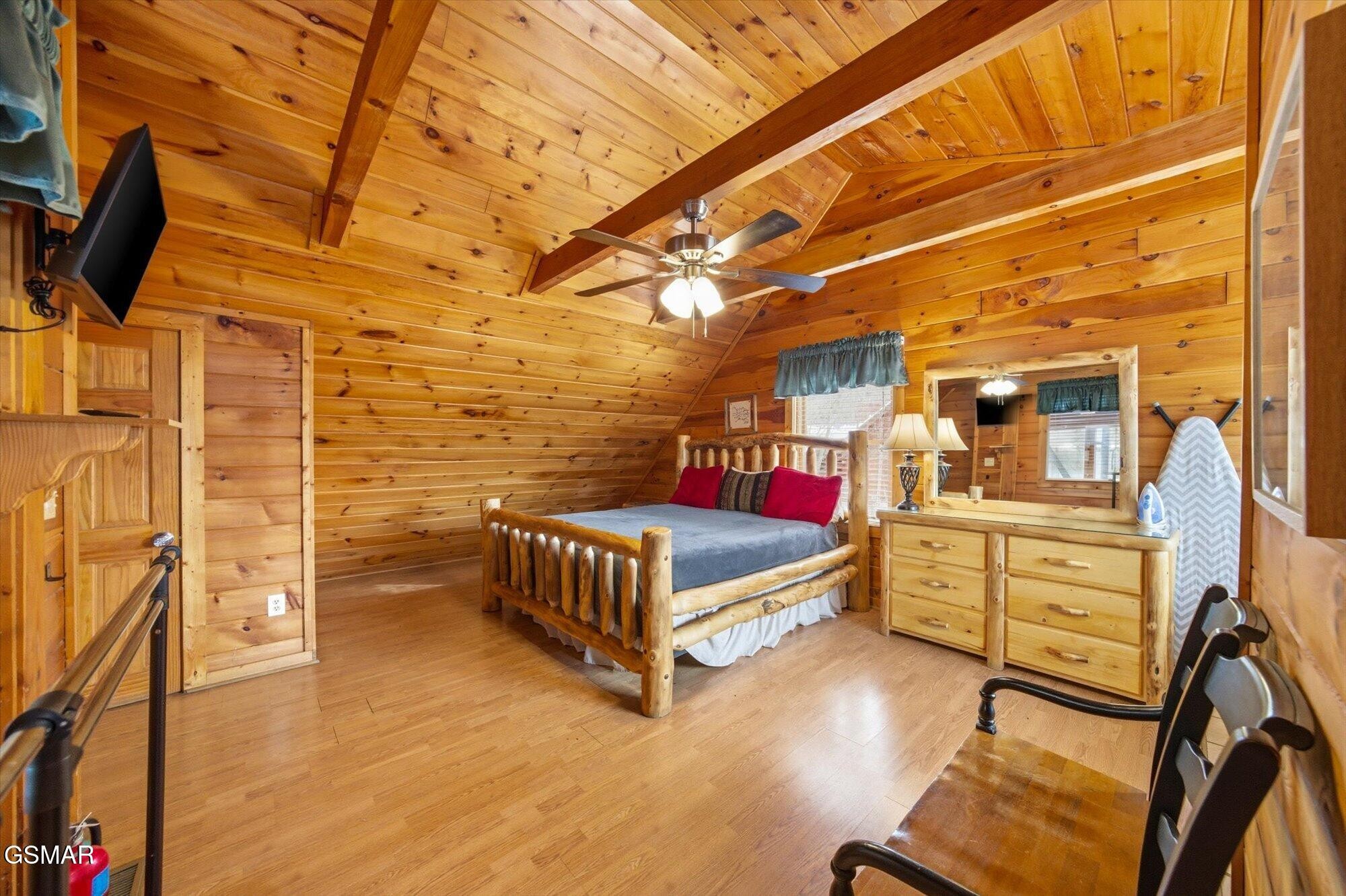 Cabin bedroom with a log bed, red pillows, and vaulted wood-beam ceiling.