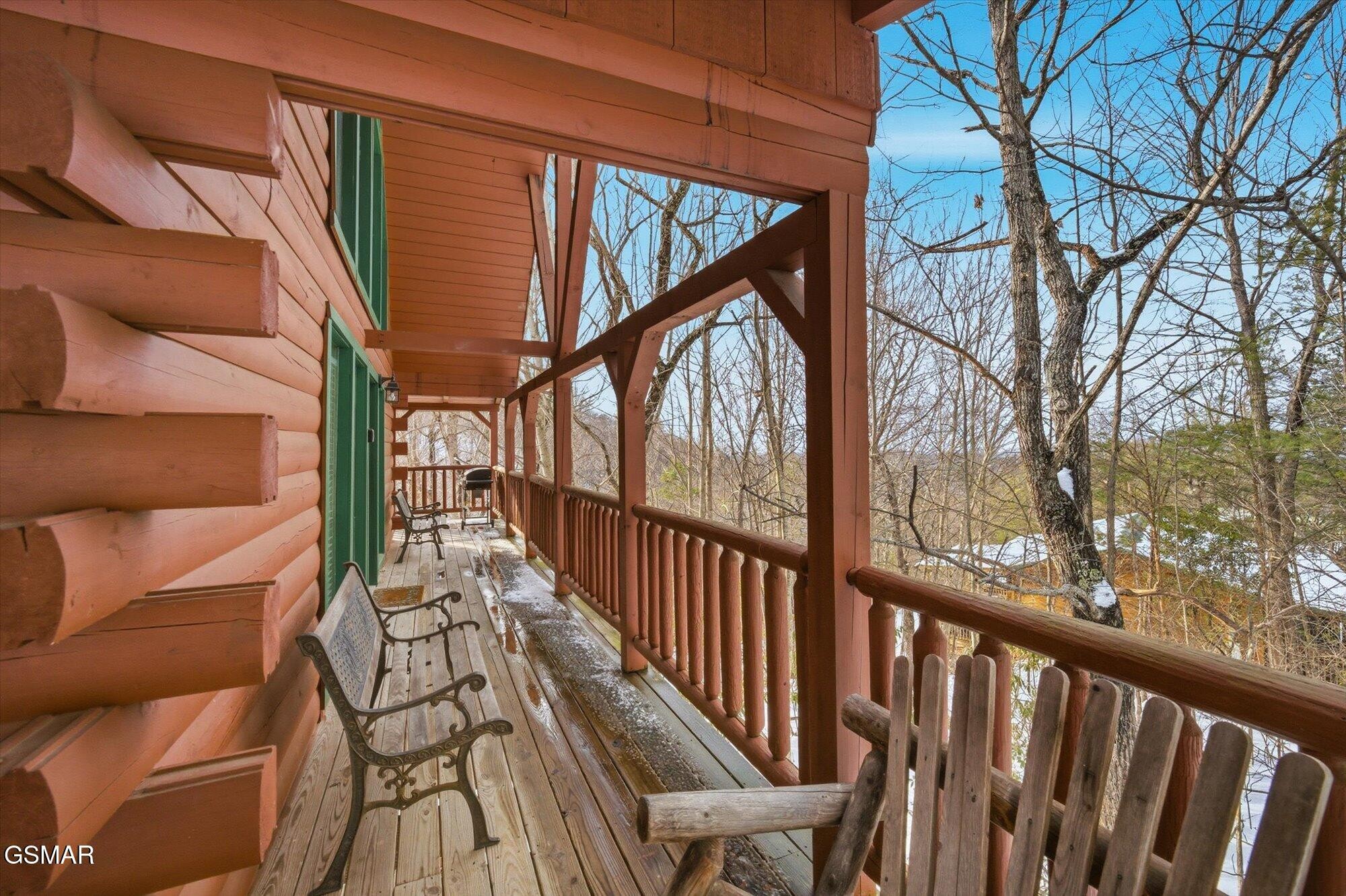 Covered log cabin porch with metal benches overlooking a snowy, leafless woodland.