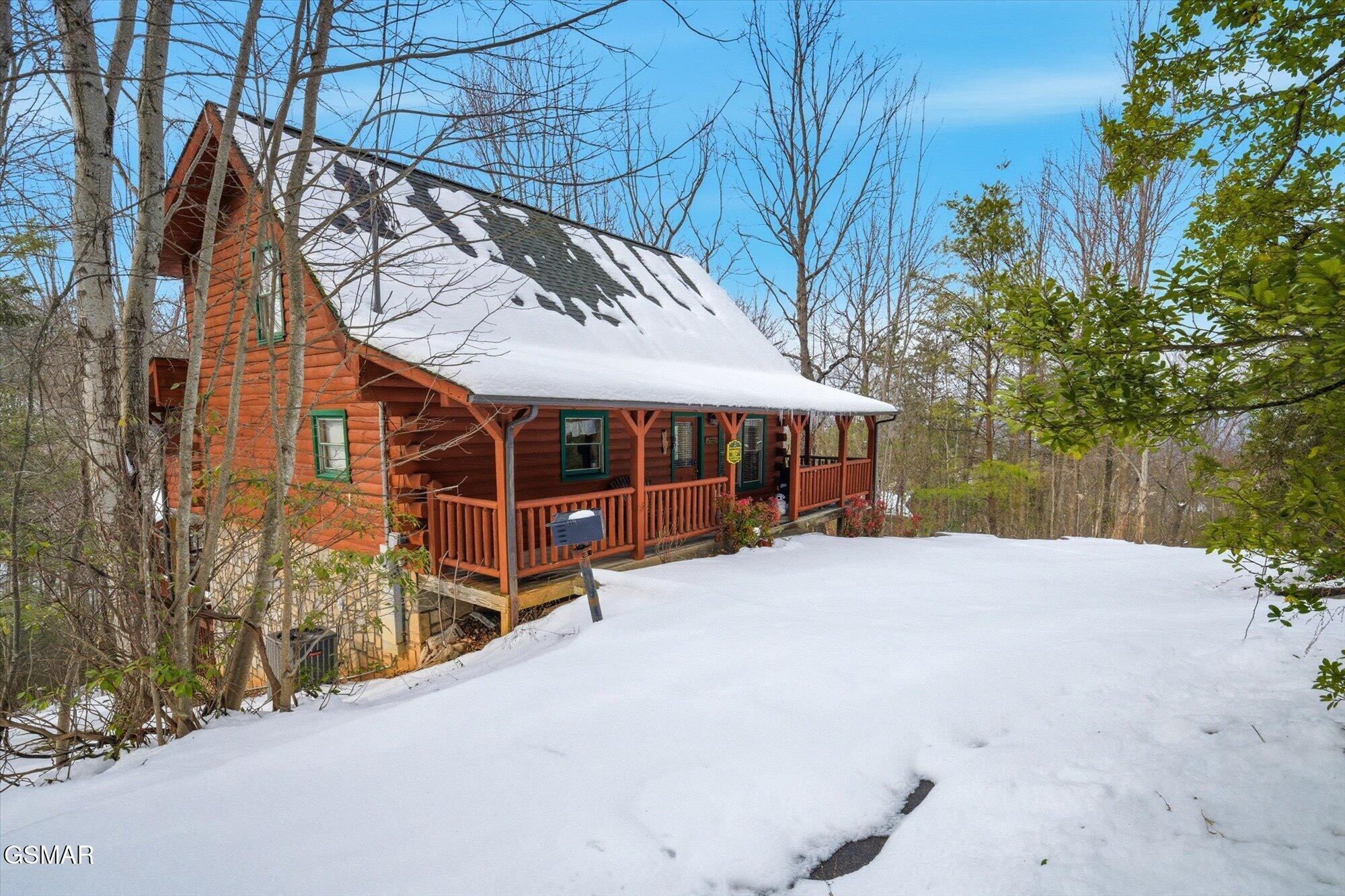 Red log cabin with a covered porch surrounded by snow and bare trees.