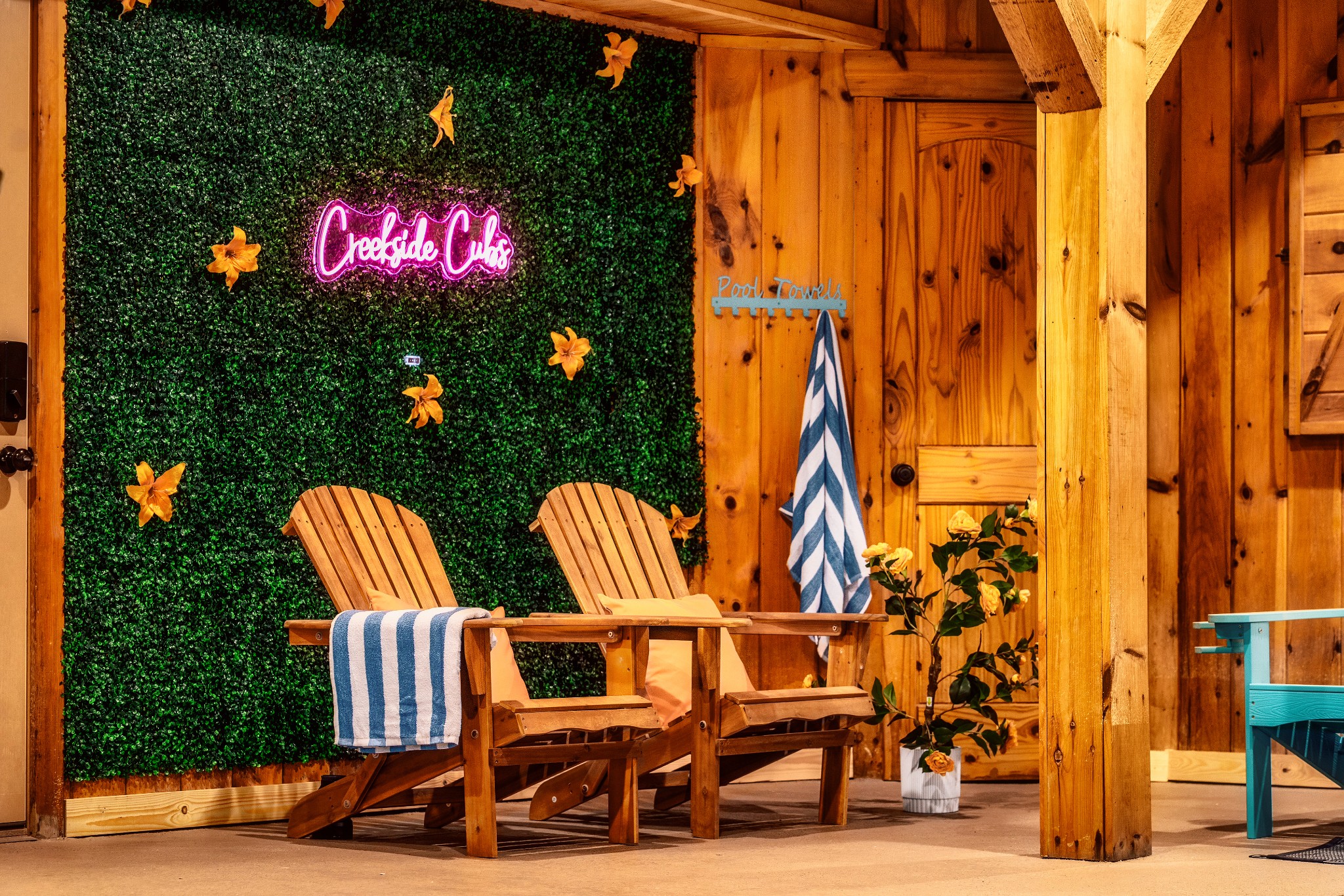 Indoor poolside seating with wooden lounge chairs, striped towels, and a pink Creekside Cubs sign.