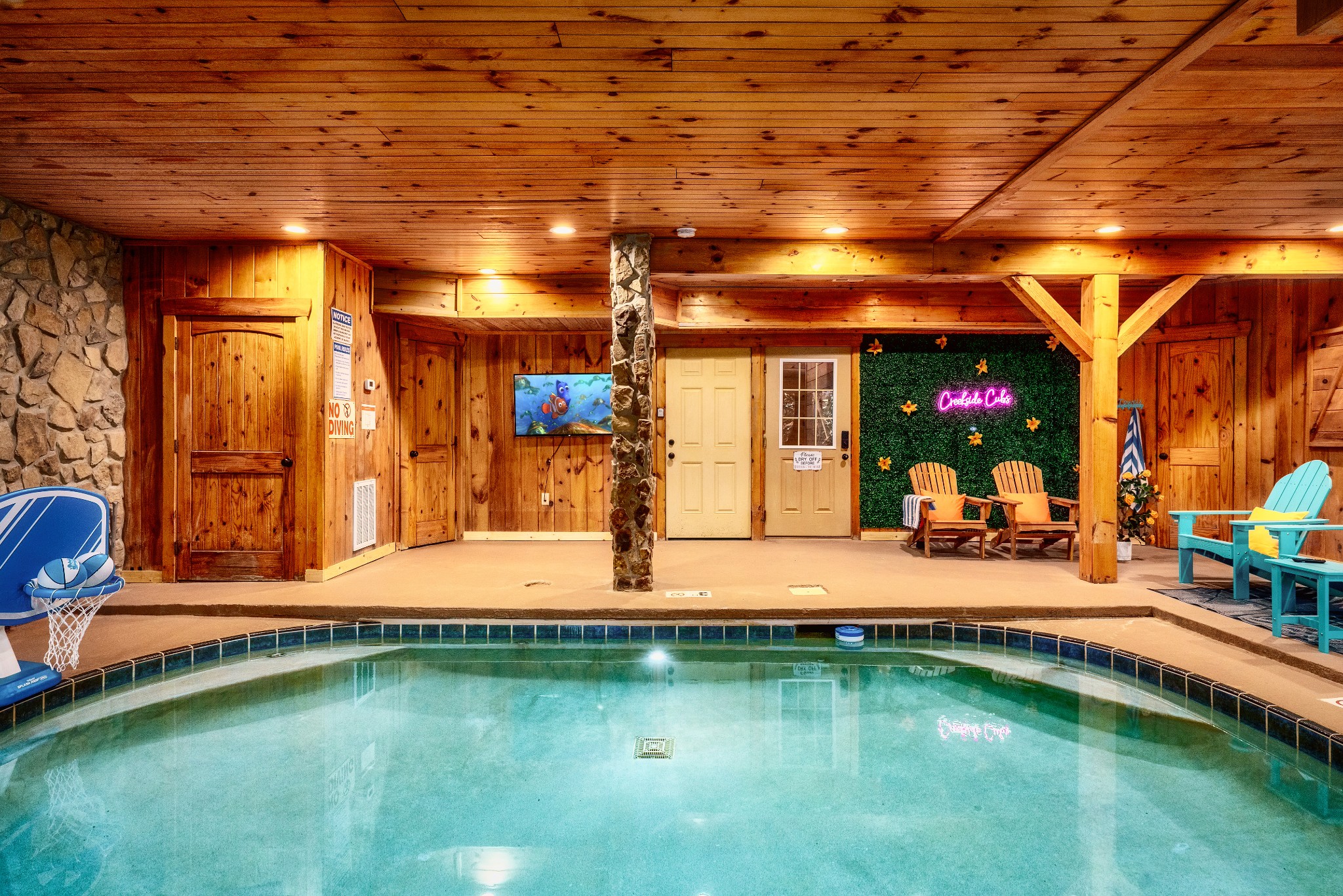 Indoor pool in a wood-paneled room with a stone column and colorful lounge chairs.