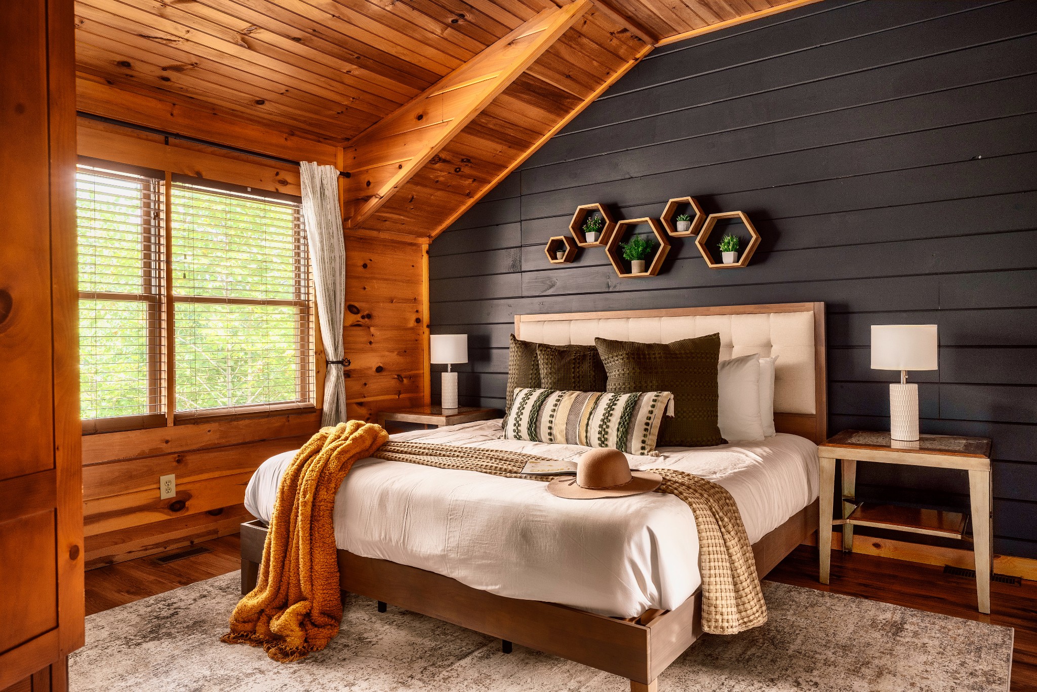 Furnished bedroom with a white bed, dark accent wall, vaulted wood ceiling, and large windows.