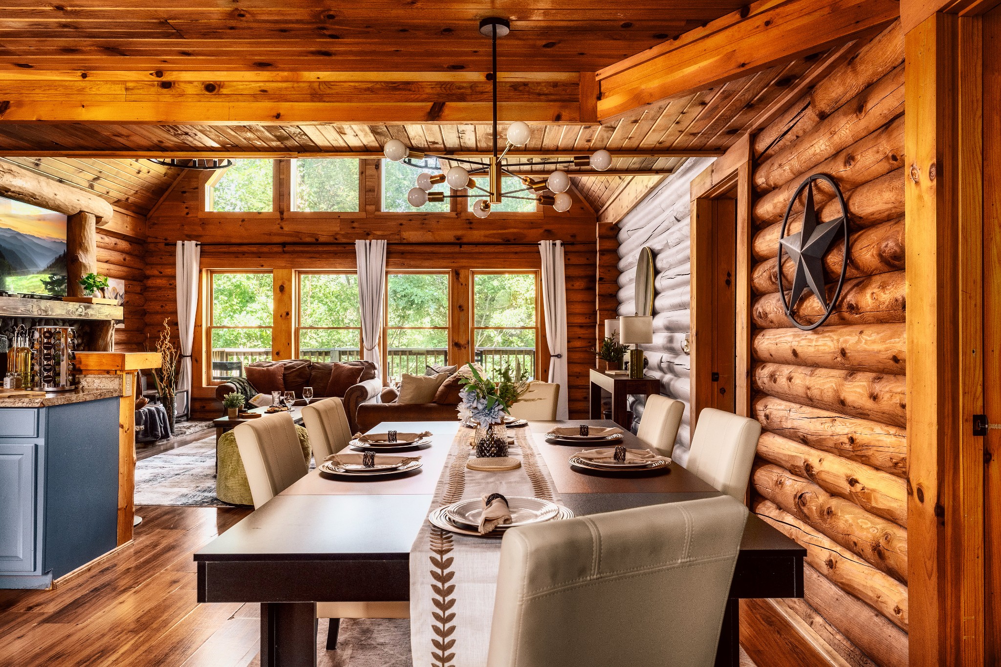 Furnished log-cabin dining and living area with a vaulted timber ceiling and large windows.
