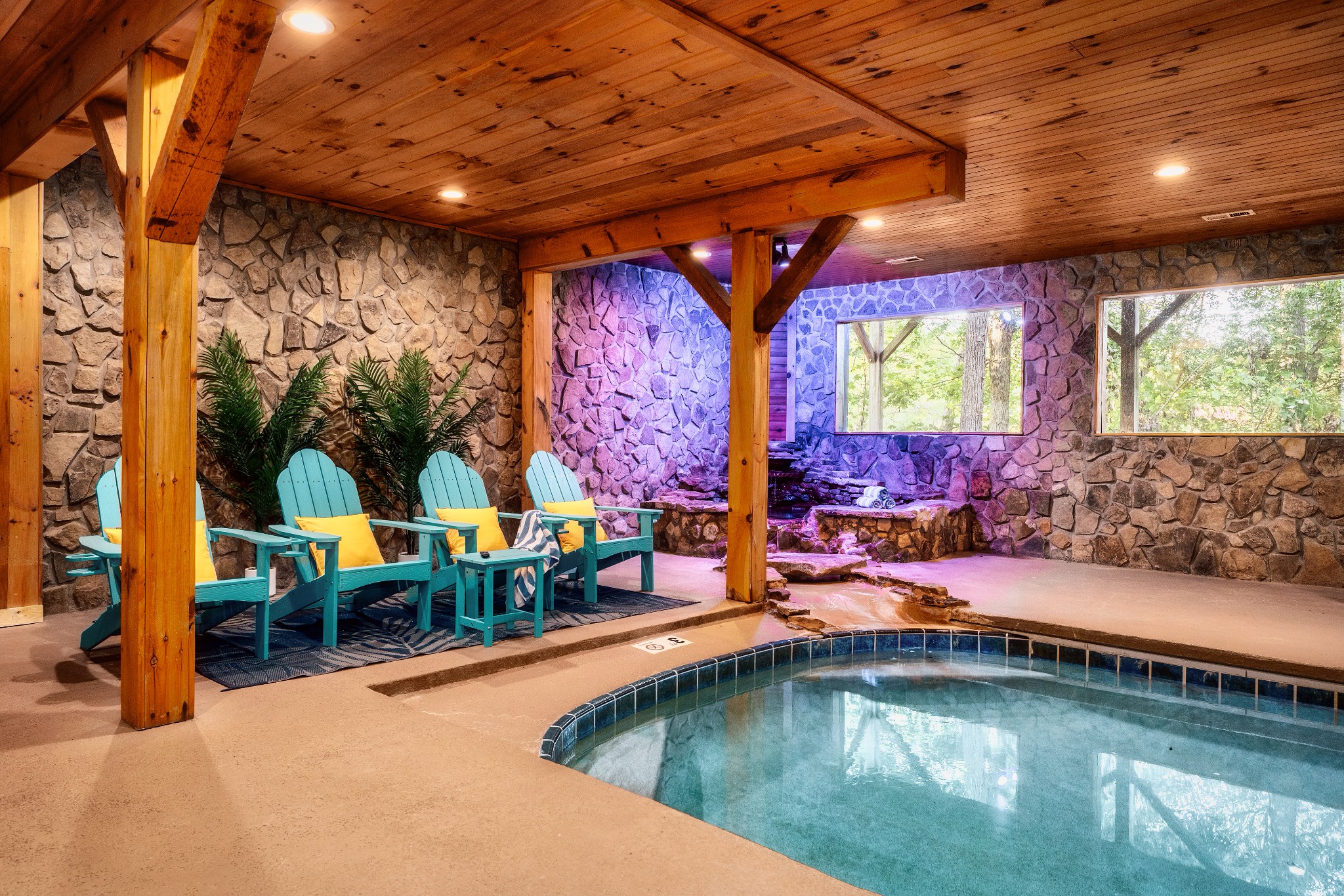 Indoor pool with stone walls, exposed timber beams, and turquoise lounge chairs.