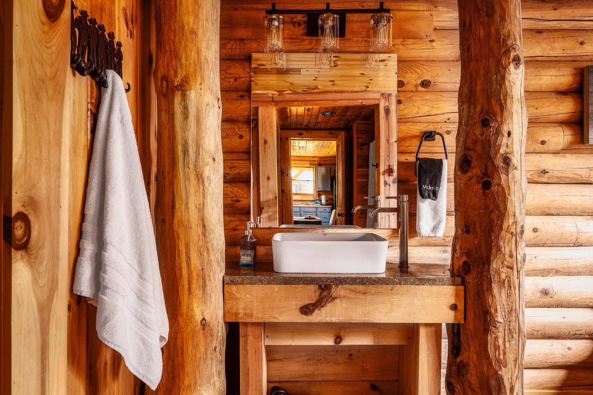 Rustic cabin bathroom vanity with a white vessel sink, wood-framed mirror, and exposed log walls.