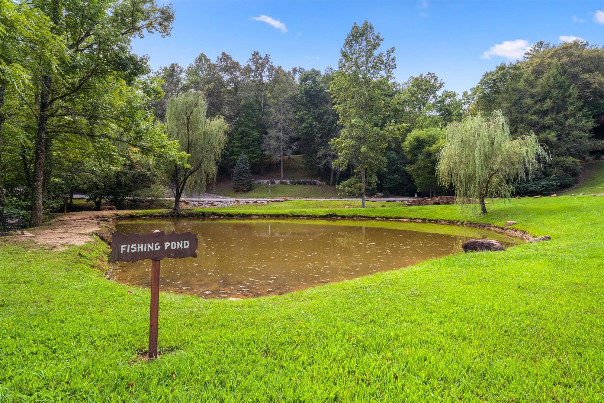 Landscaped fishing pond edged by green lawn and mature trees, with a Fishing Pond sign.