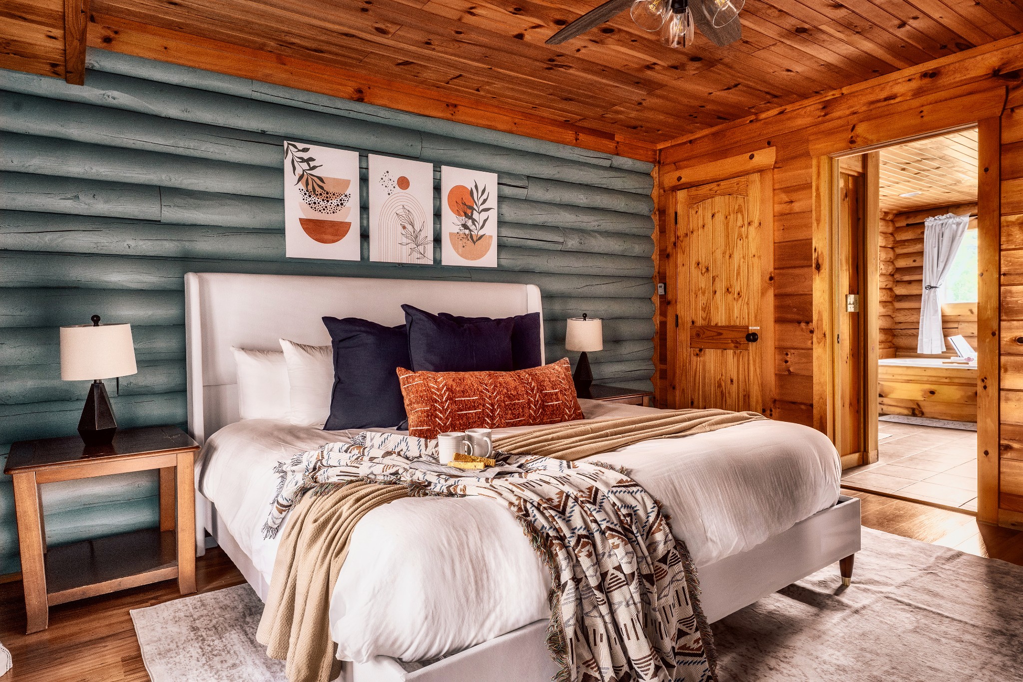 Cabin bedroom with a white bed, blue-gray log walls, and a wood ceiling.
