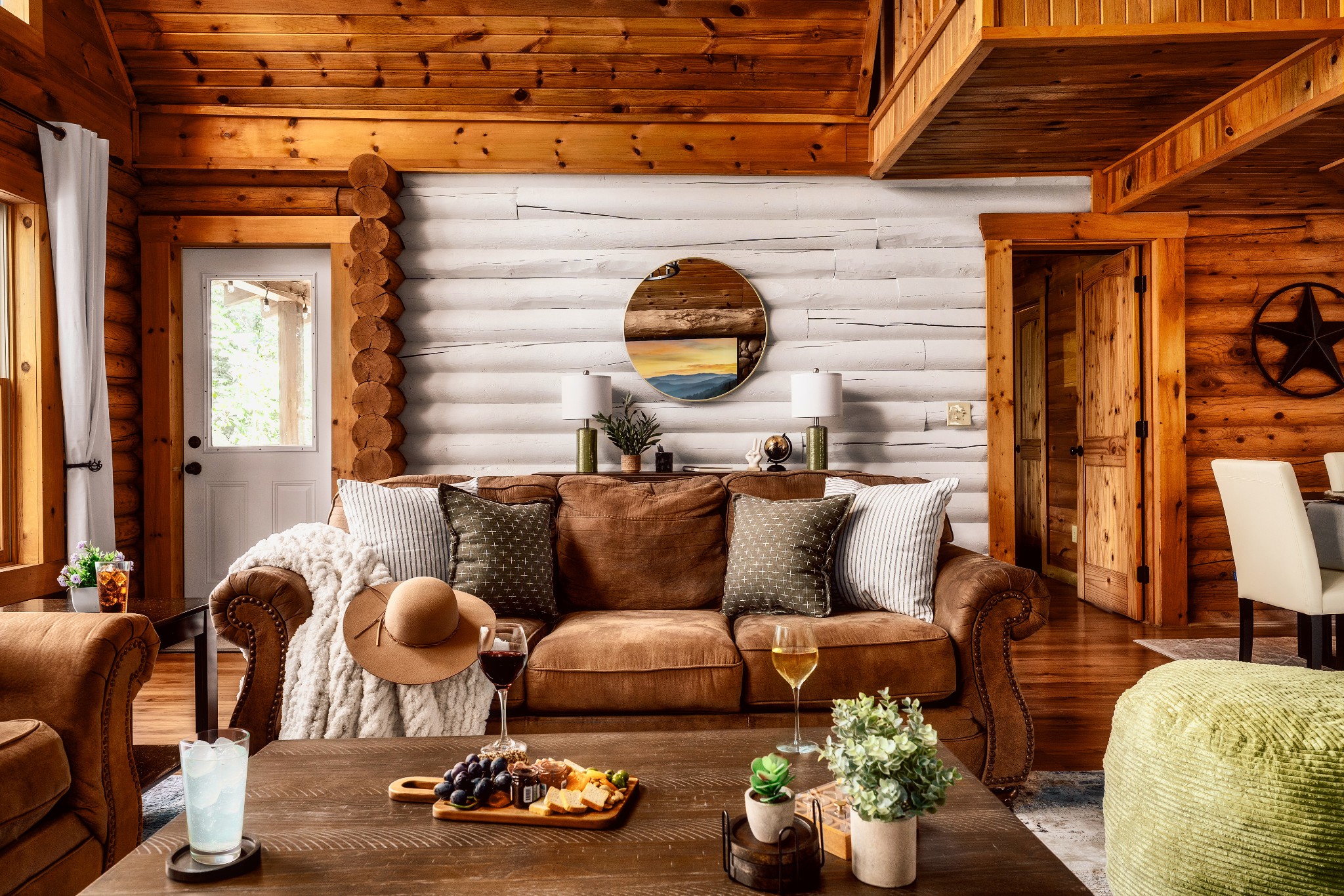 Log-cabin living room with a brown leather sofa, whitewashed log wall, and exposed timber ceiling.