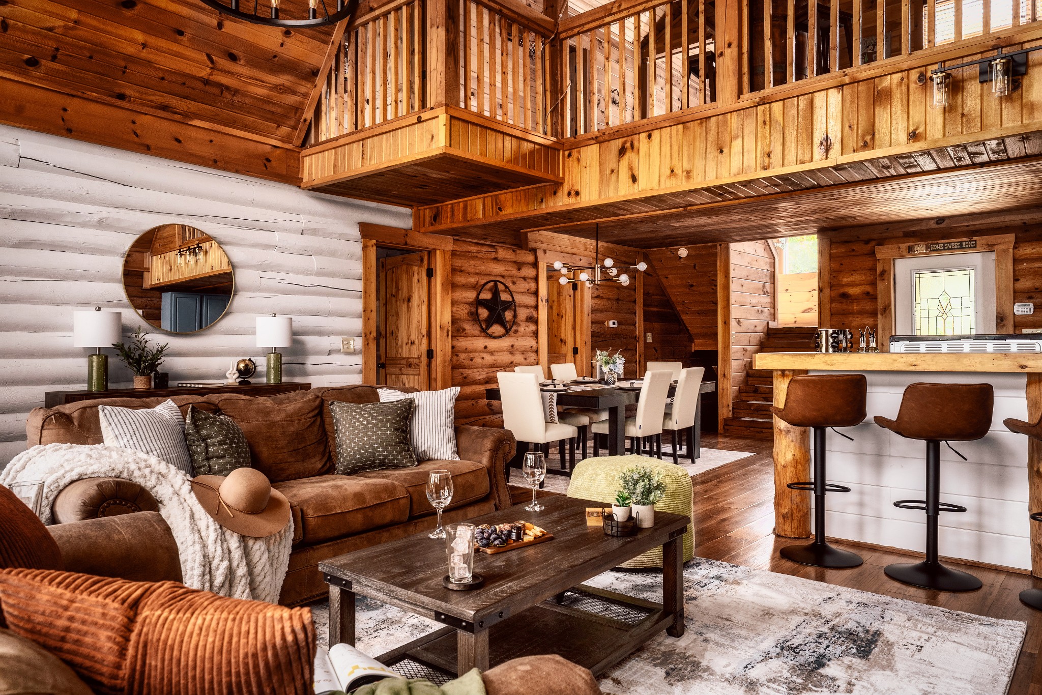 Rustic cabin great room with a vaulted wood ceiling, loft, brown sofa, dining table, and kitchen island.