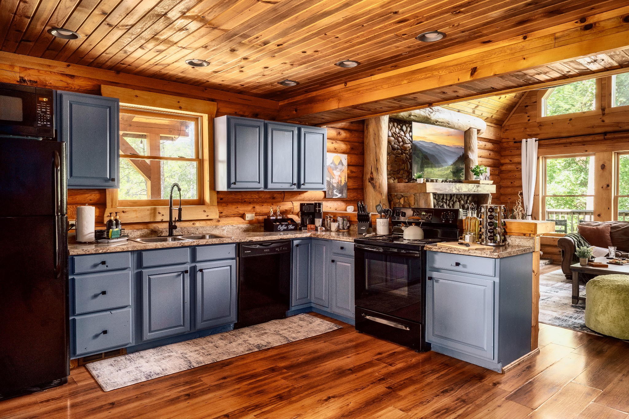 Rustic cabin kitchen with blue-gray cabinets, granite counters, and a stone fireplace behind the range.