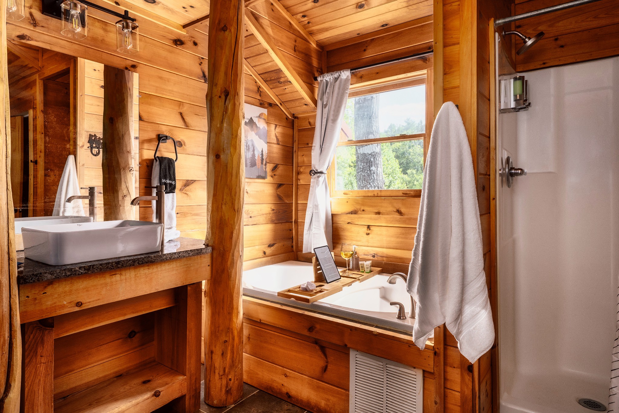 Cabin bathroom with a soaking tub beneath a window and a vessel sink on a stone counter.