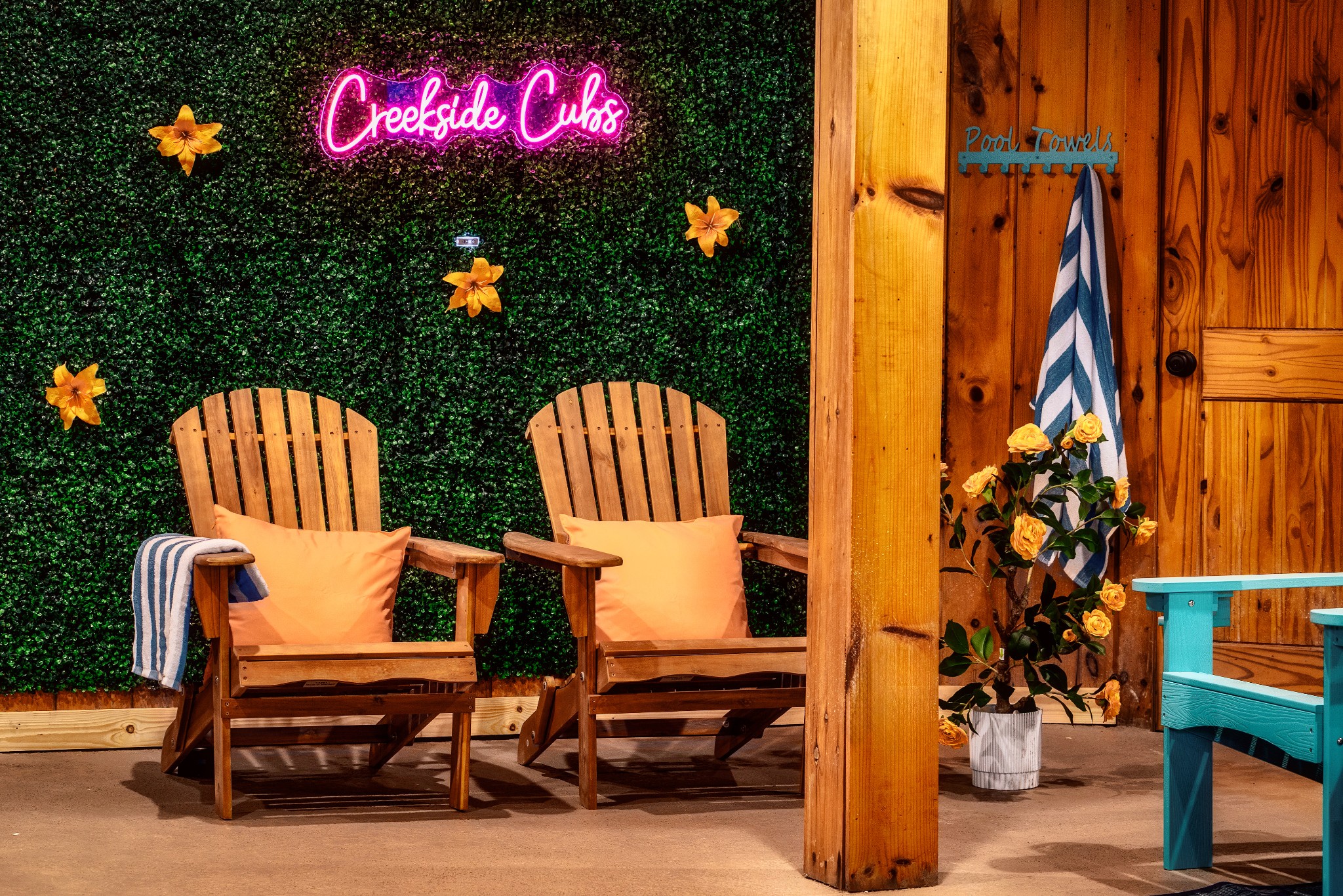 Poolside patio with wooden Adirondack chairs, a Creekside Cubs neon sign, and a pool-towel hook.