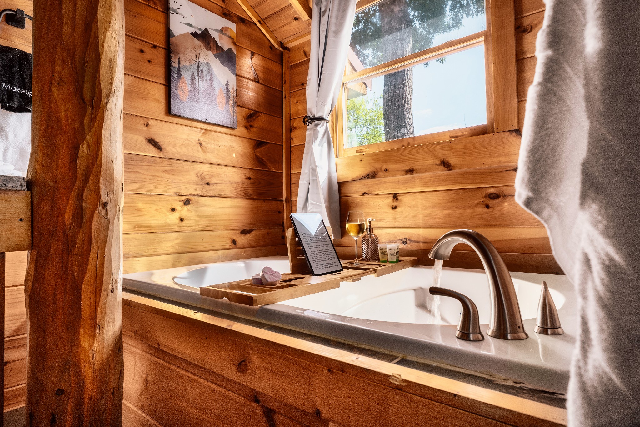 Soaking tub in a wood-paneled bathroom, with a bath tray and large sunlit window.