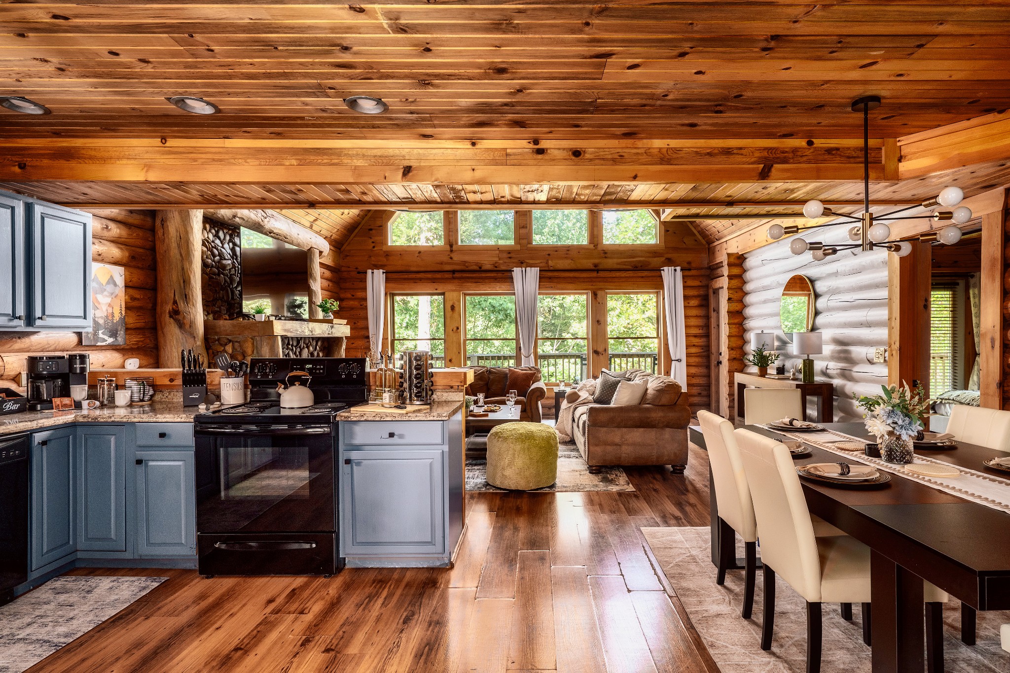 Open-plan log cabin kitchen, dining, and living area with blue cabinets and a stone fireplace.