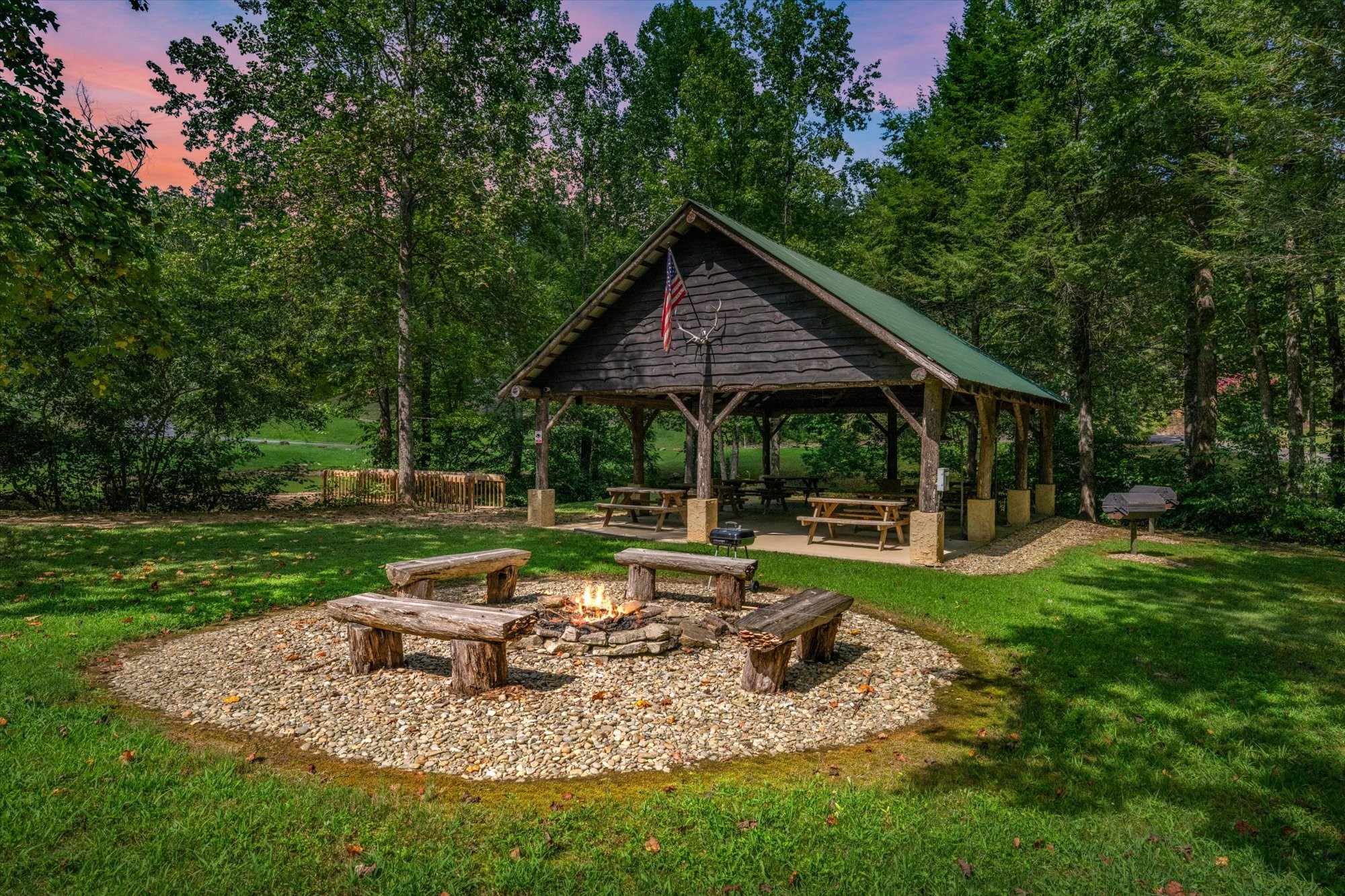 Wooded picnic pavilion beside a stone fire pit ringed with log benches.