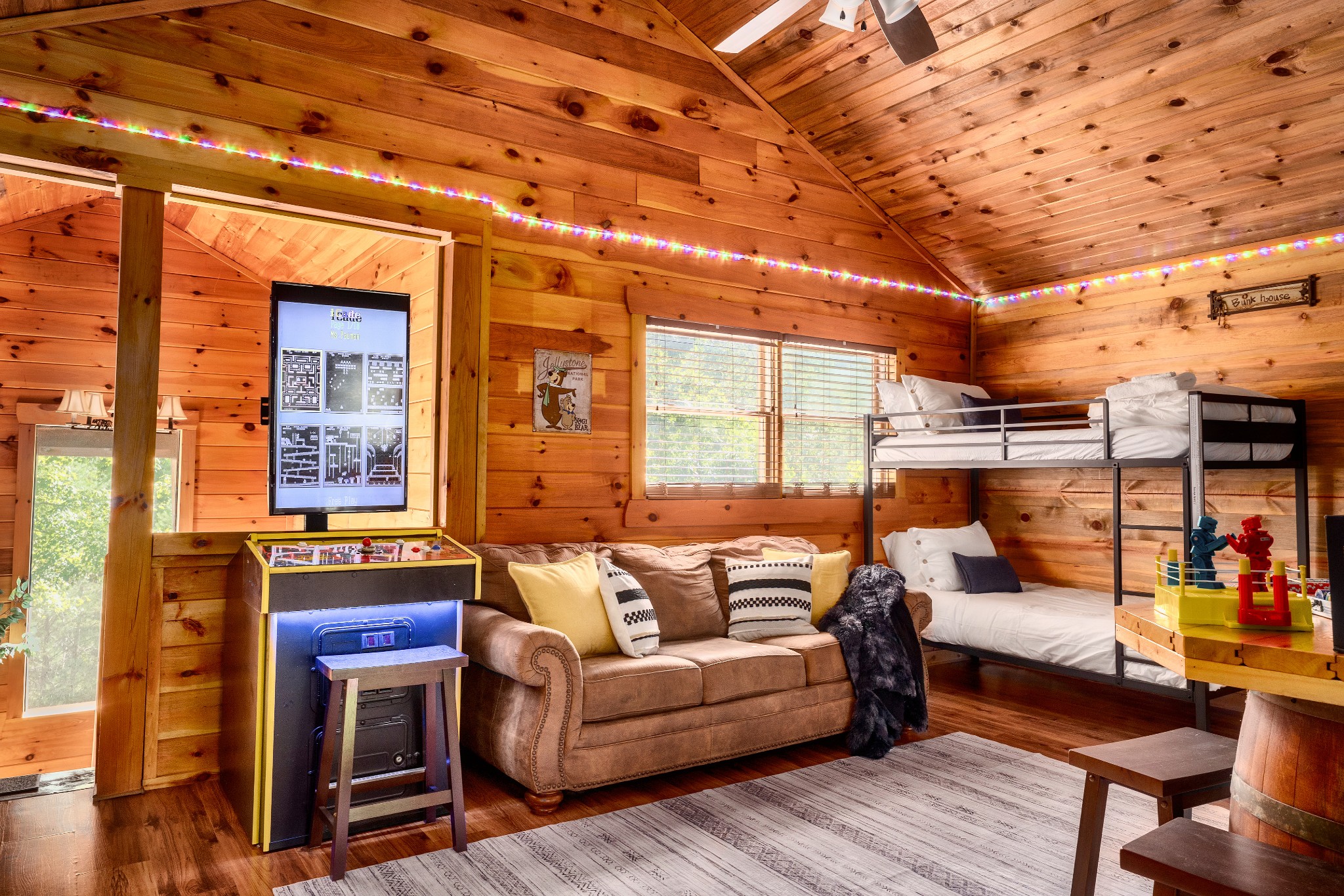 Wood-paneled bunk room with a metal bunk bed, brown sofa, and pinball machine.