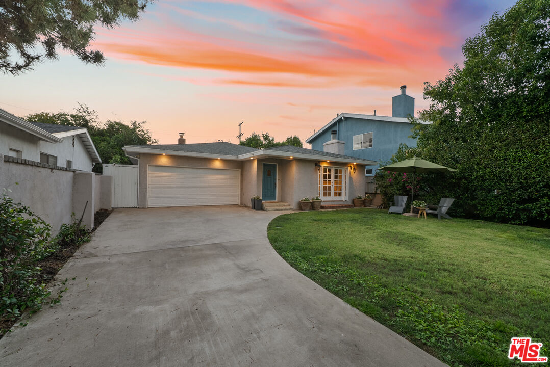 Single-story home with a wide driveway and lawn beneath a pink-orange dusk sky.