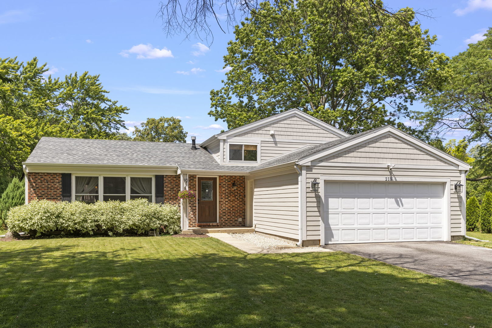 Split-level home with brick entry, light siding, and attached two-car garage.