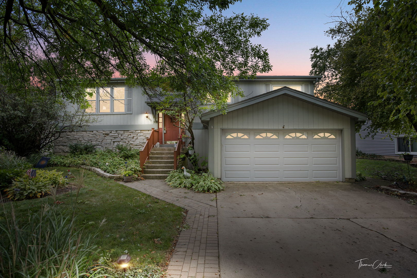 Two-story gray home with a stone facade, red front door, and attached garage at dusk.