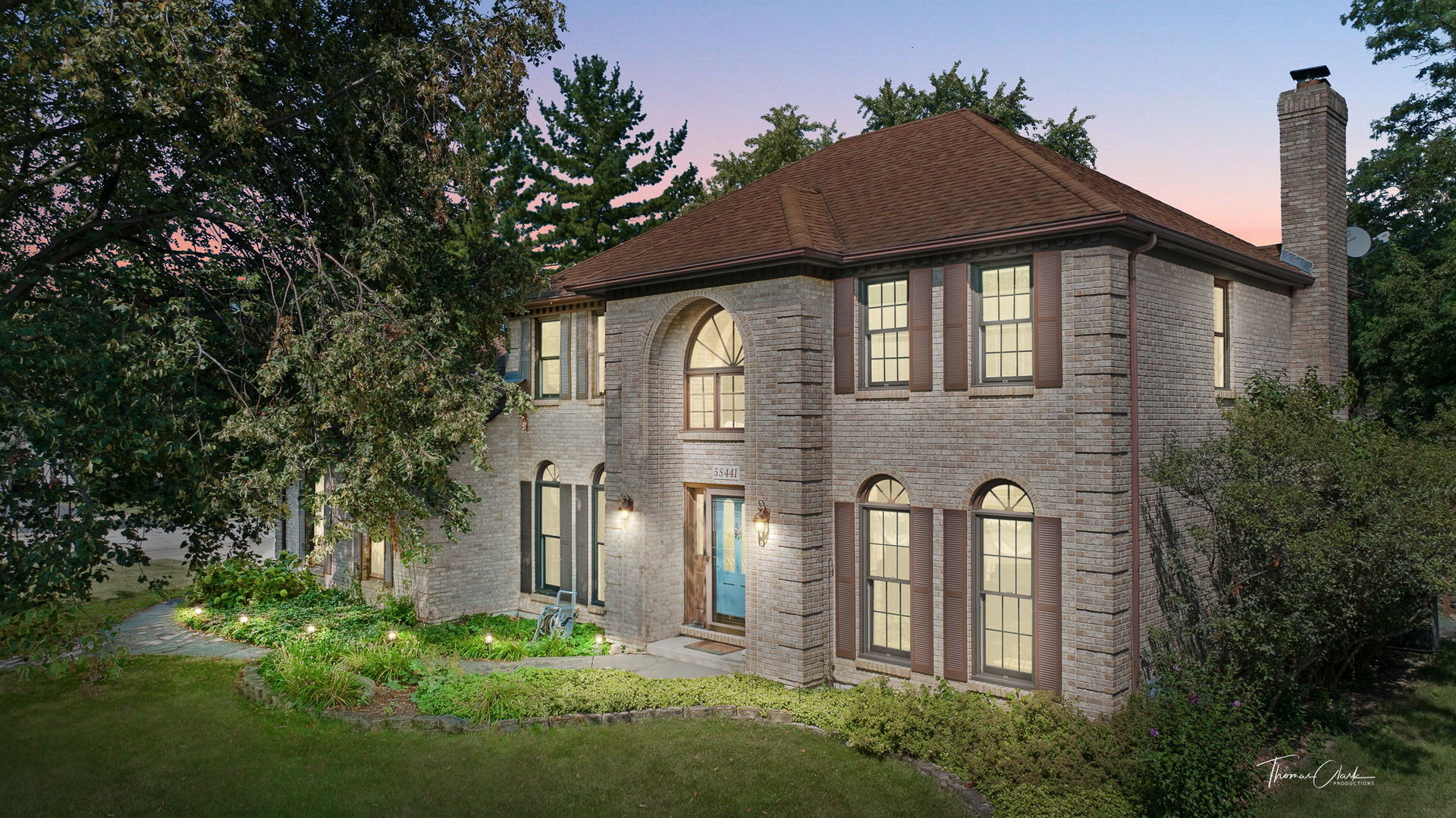 Two-story brick home with arched windows, a blue front door, and a landscaped walkway at dusk.