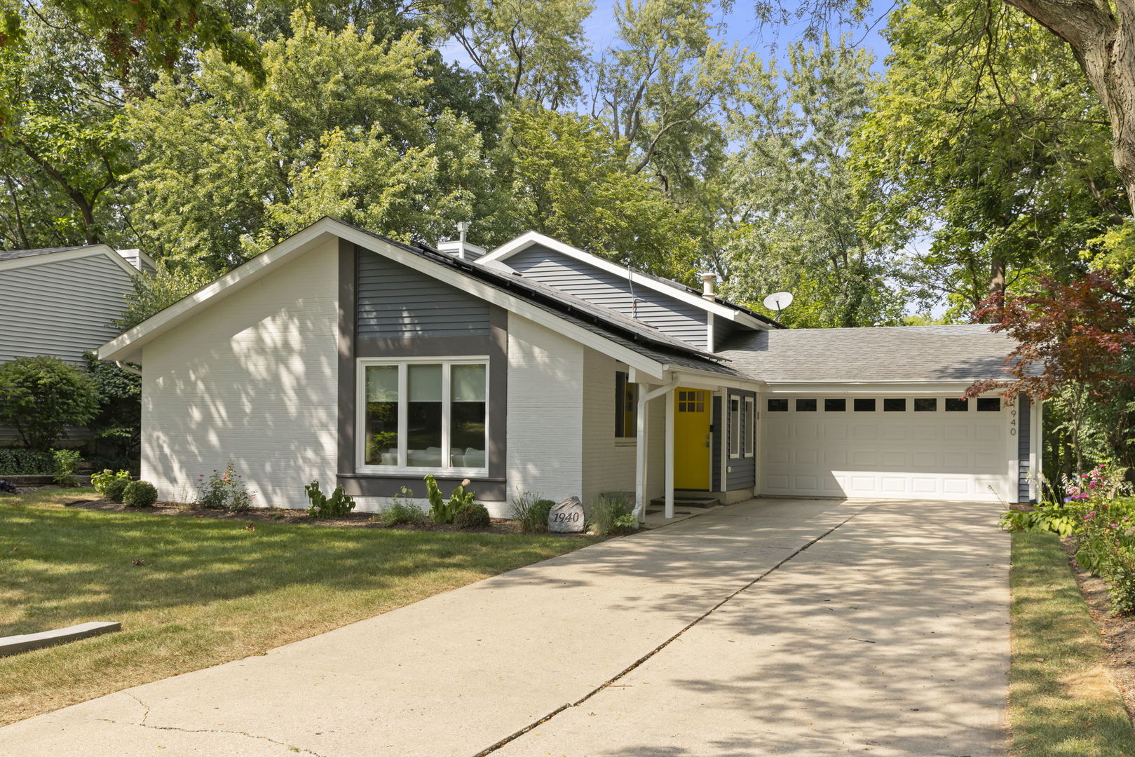 Single-story home with a yellow front door, attached two-car garage, and mature trees.