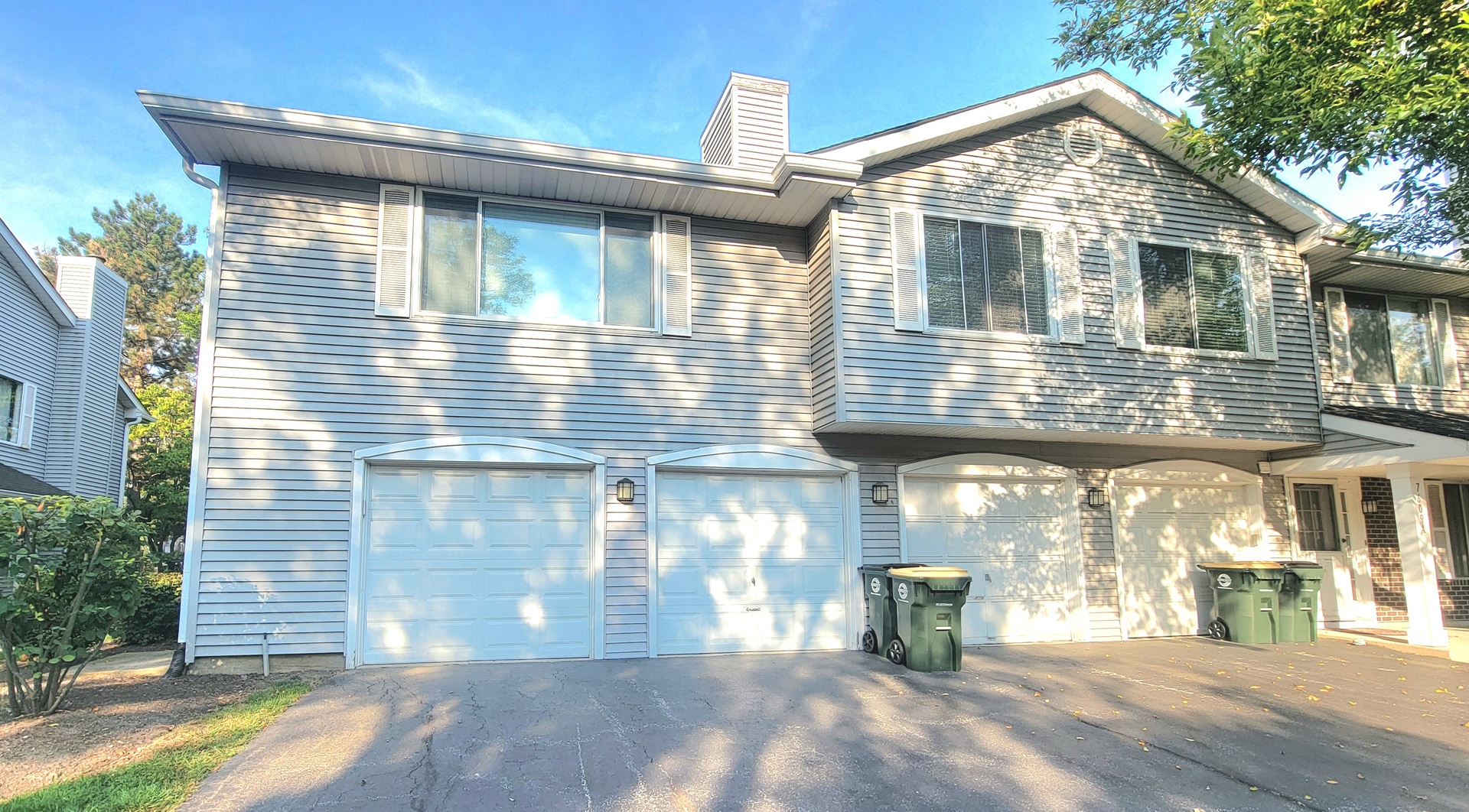 Gray-sided attached townhome with white trim, multiple garage doors, and a paved driveway.