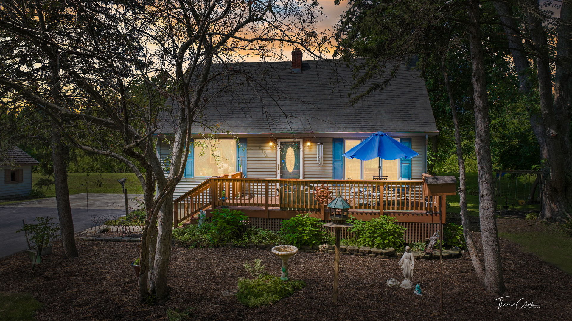 House with a wooden backyard deck, blue patio umbrella, and mature trees at dusk.