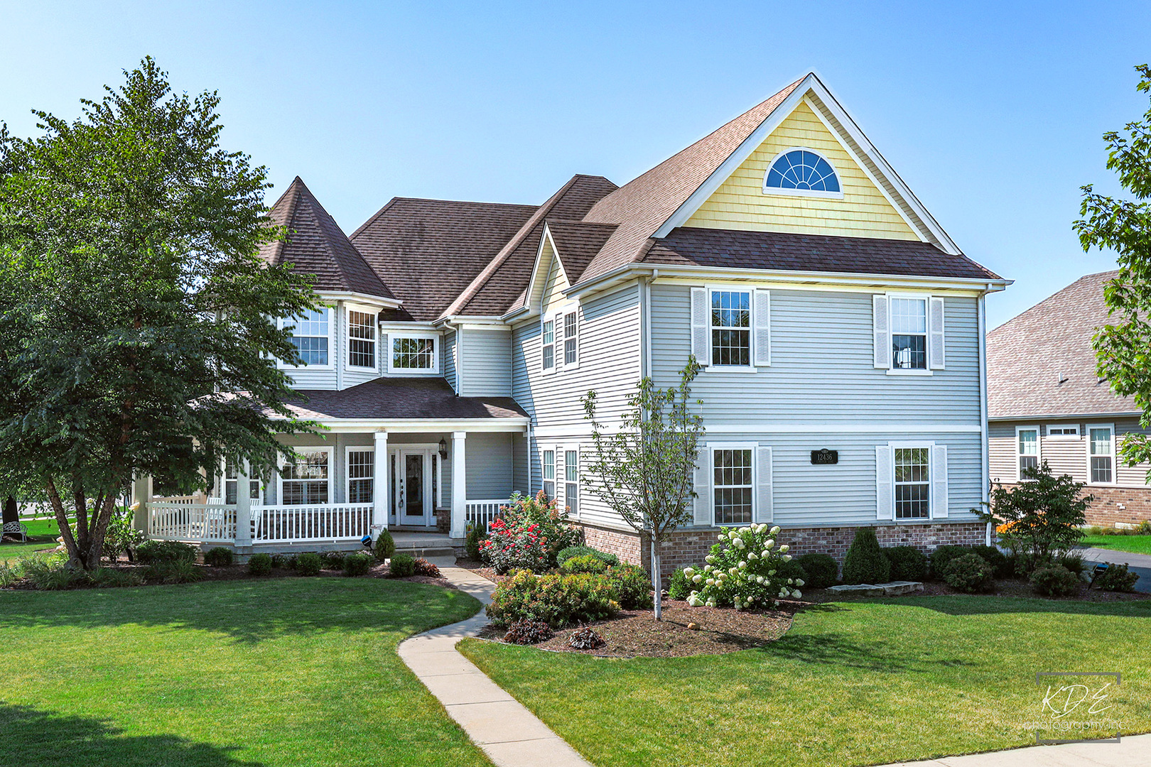 Two-story blue house with steep gables, a covered porch, landscaped garden, and curved walkway.