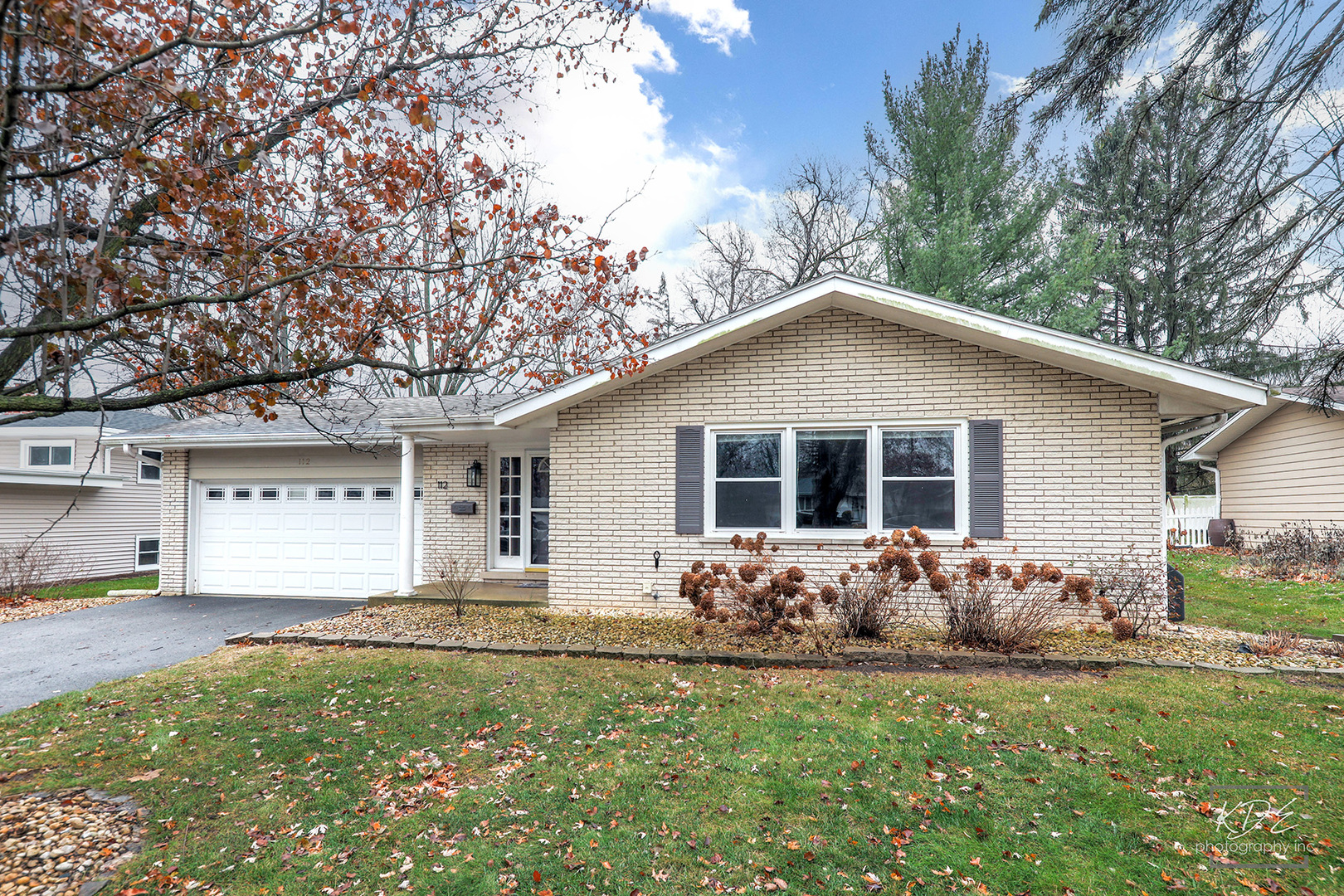 Single-story brick ranch home with attached garage, framed by autumn trees and a leaf-strewn lawn.