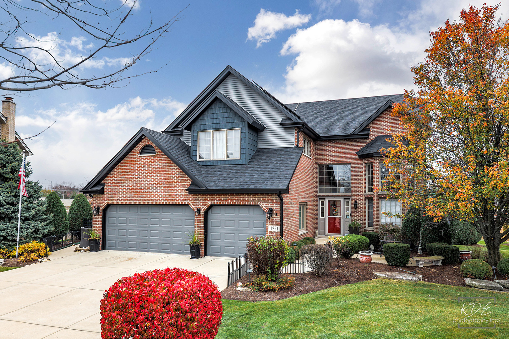 Brick two-story home with dual garages, a landscaped yard, and autumn foliage.