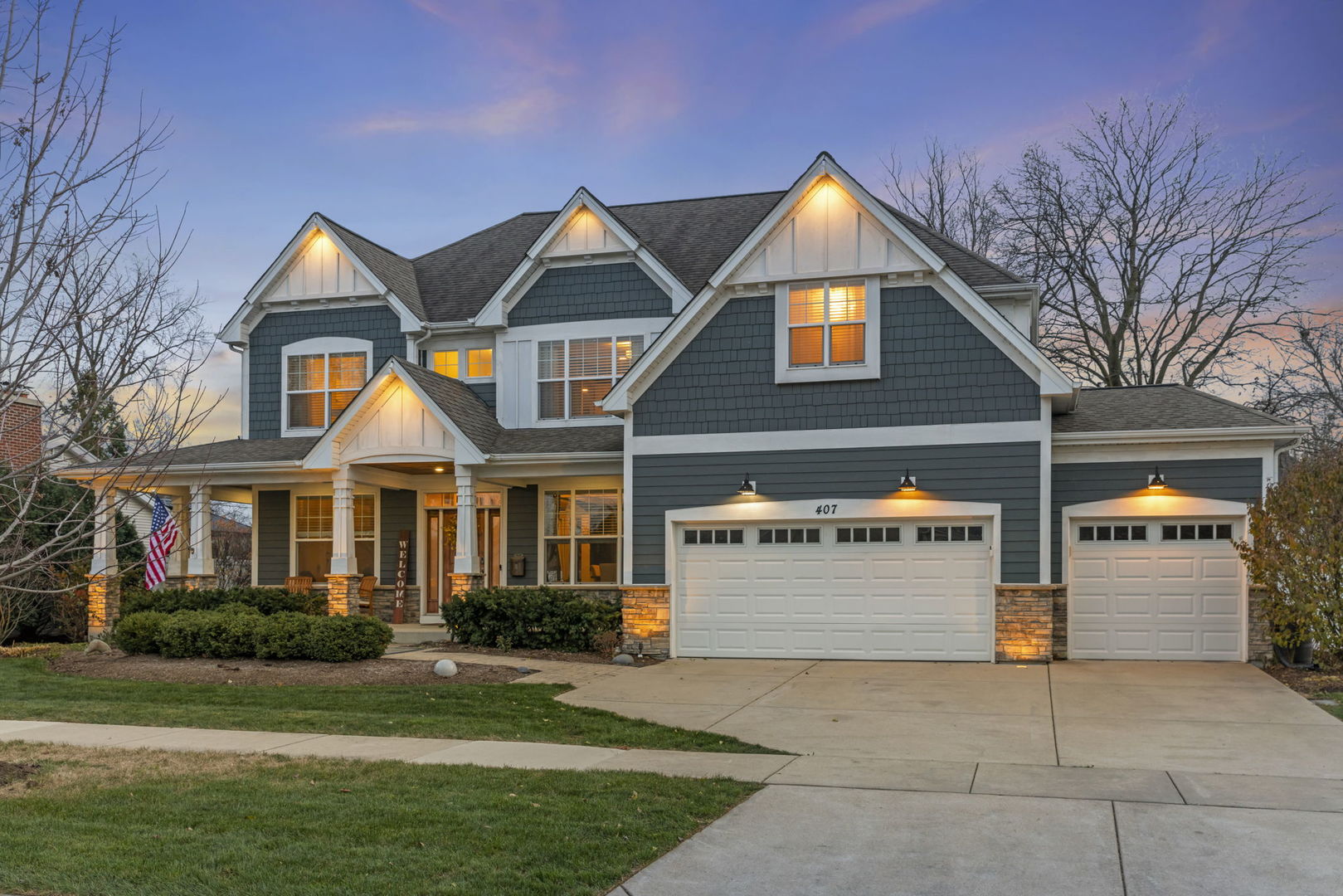 Two-story blue home with white trim, a covered porch, and a three-car garage at dusk.