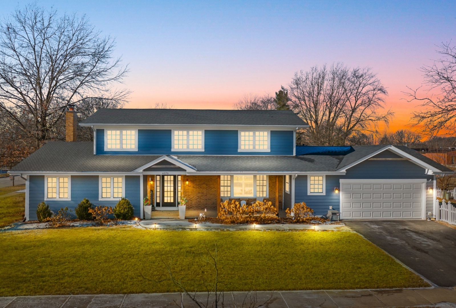 Blue-sided home with brick entry and attached garage, photographed at sunset.
