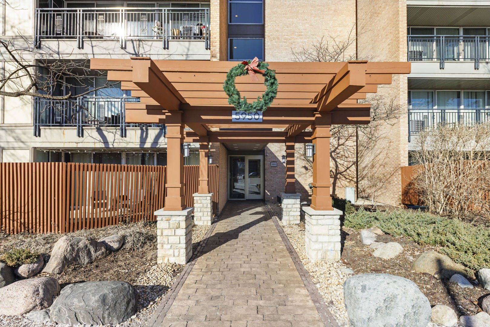 Residential building entrance beneath a wooden pergola with a holiday wreath and a 5950 sign.