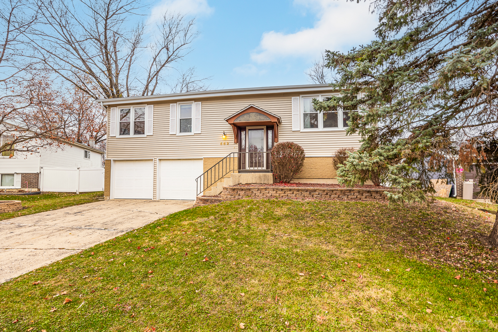 Beige split-level home with a double garage, raised entrance, and sloping front lawn.