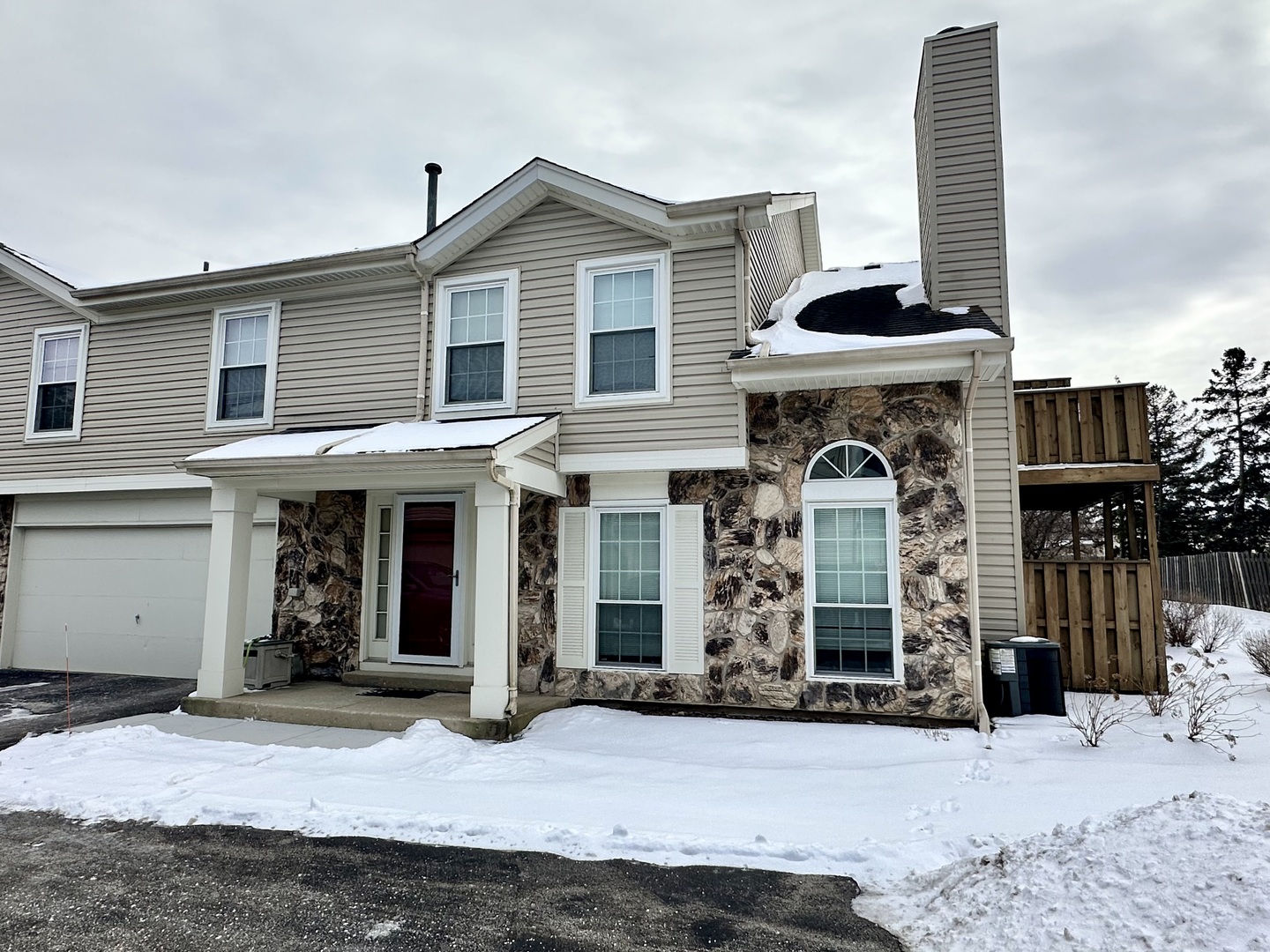 Two-story house with a stone facade, attached garage, and raised deck surrounded by snow.