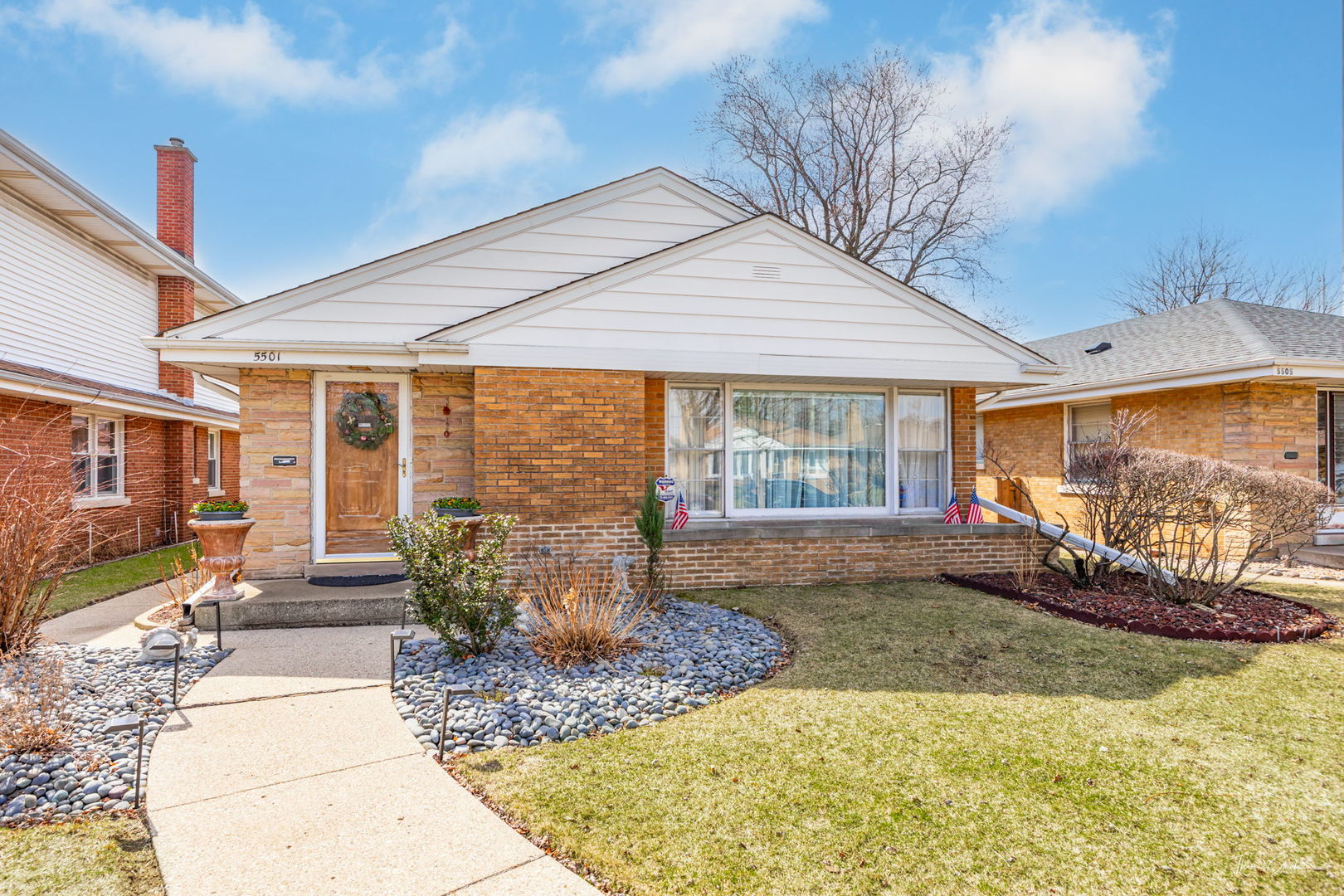 Single-story brick house with a white gabled roof and landscaped front yard.