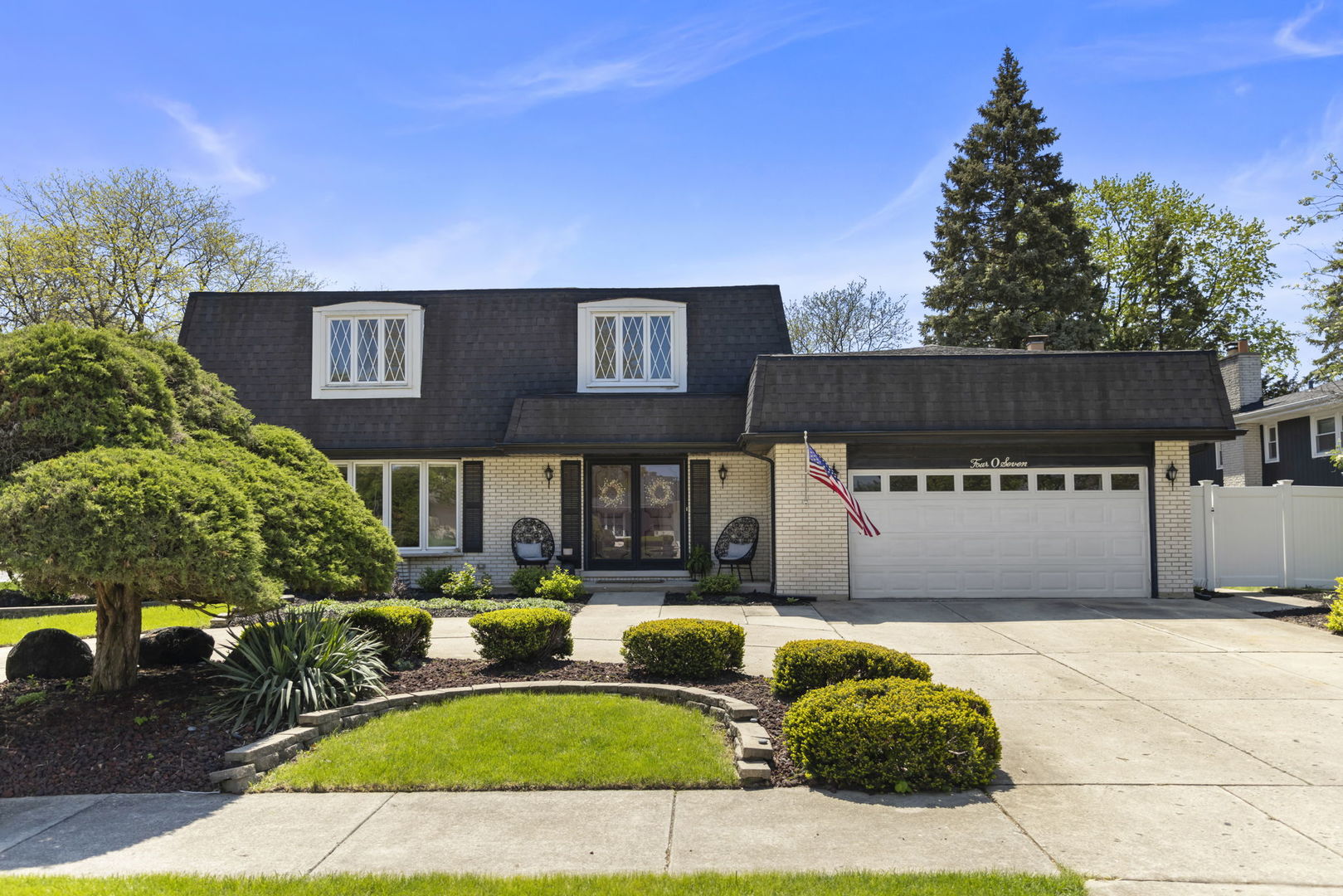 Light brick home with two dormers, an attached garage, and a landscaped front yard.