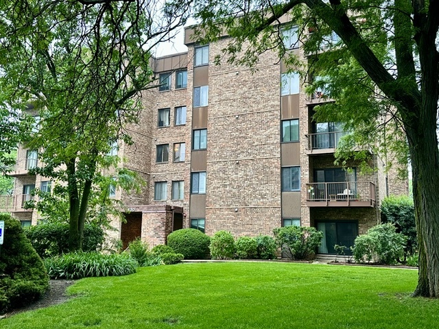 Brick condominium building with balconies, framed by mature trees and a manicured lawn.