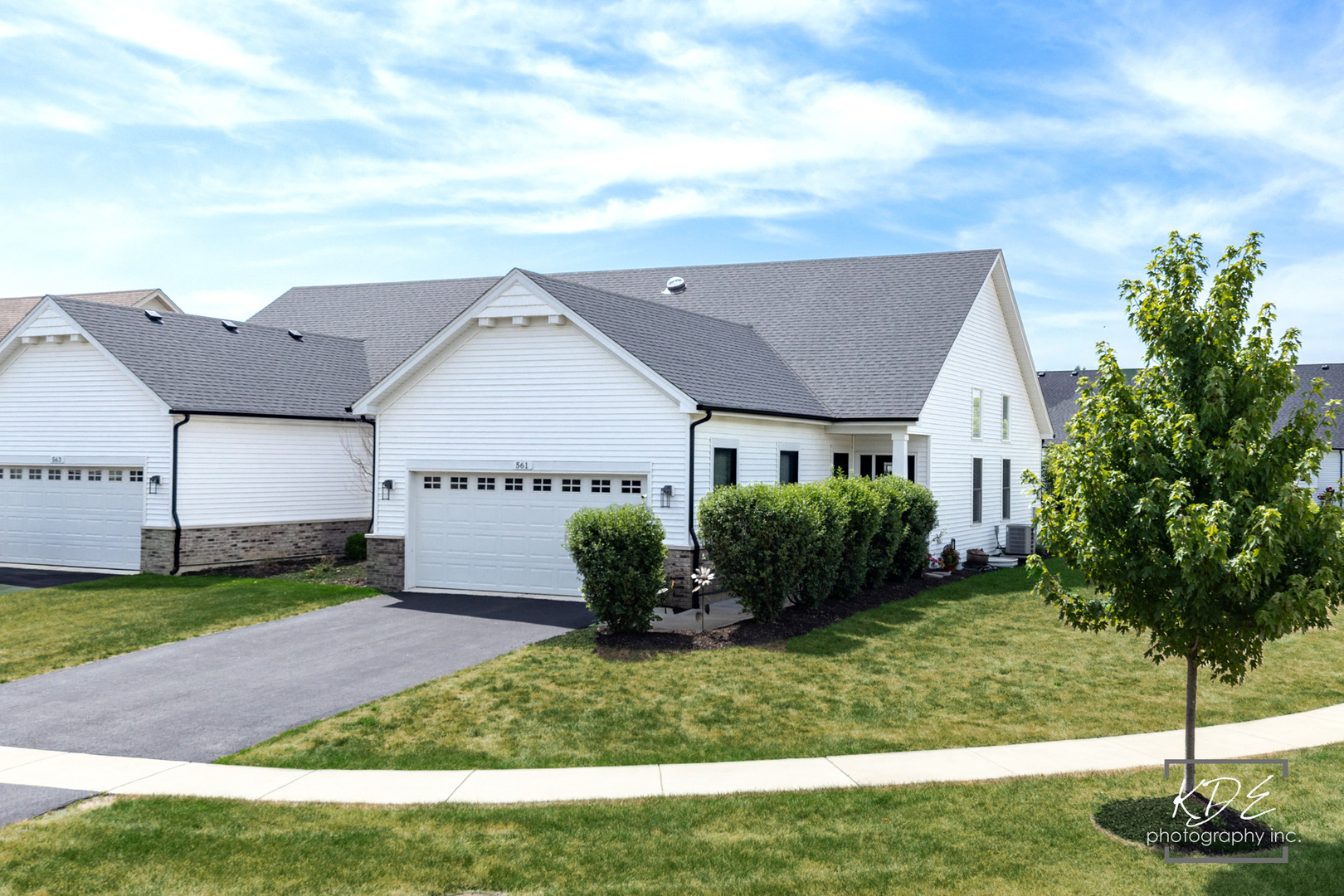 White-sided home with a gabled roof, attached garage, driveway, and landscaped lawn.
